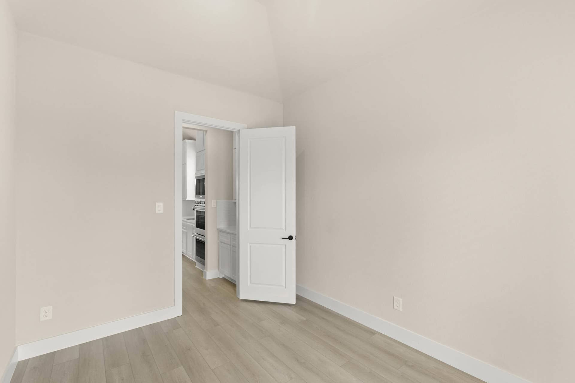 Minimalist dining room with hardwood floors and open door to kitchen.