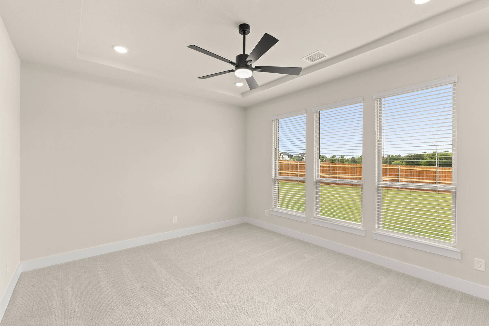 Spacious primary suite with ceiling fan and large windows overlooking the backyard.
