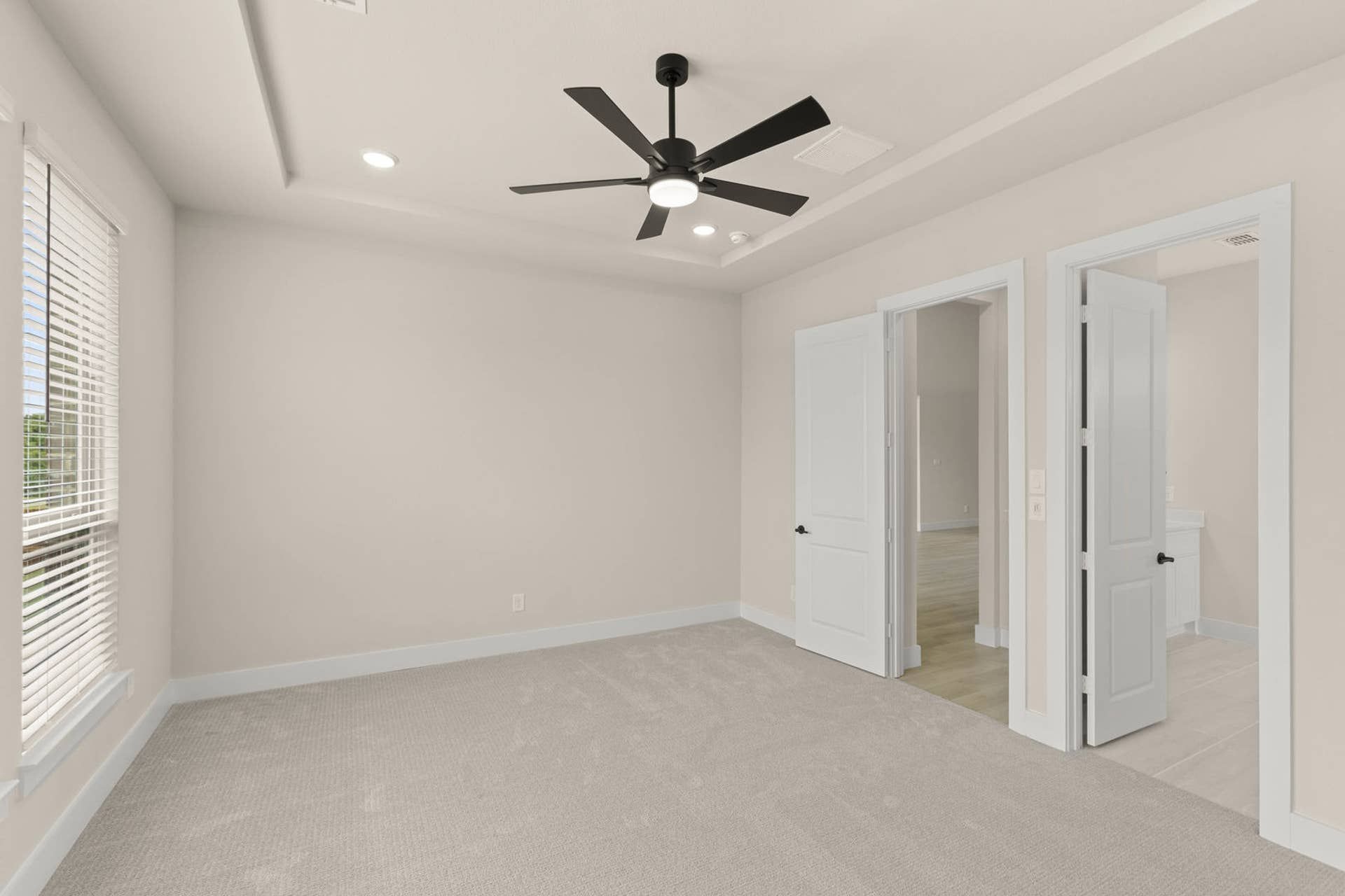 Spacious primary suite with ceiling fan and carpet flooring.