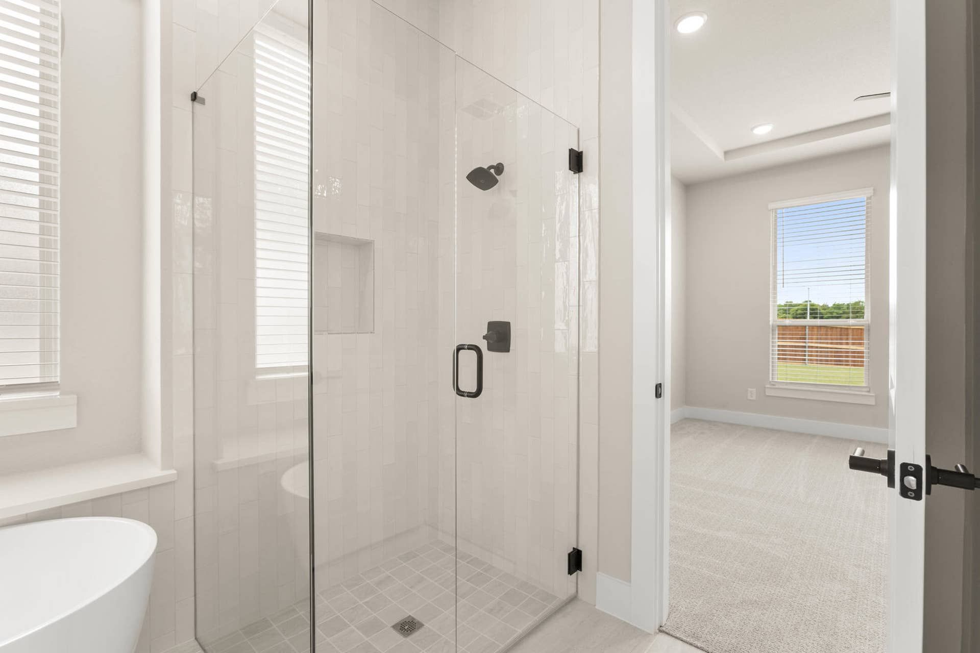 Modern bathroom with glass shower and adjacent carpeted bedroom.