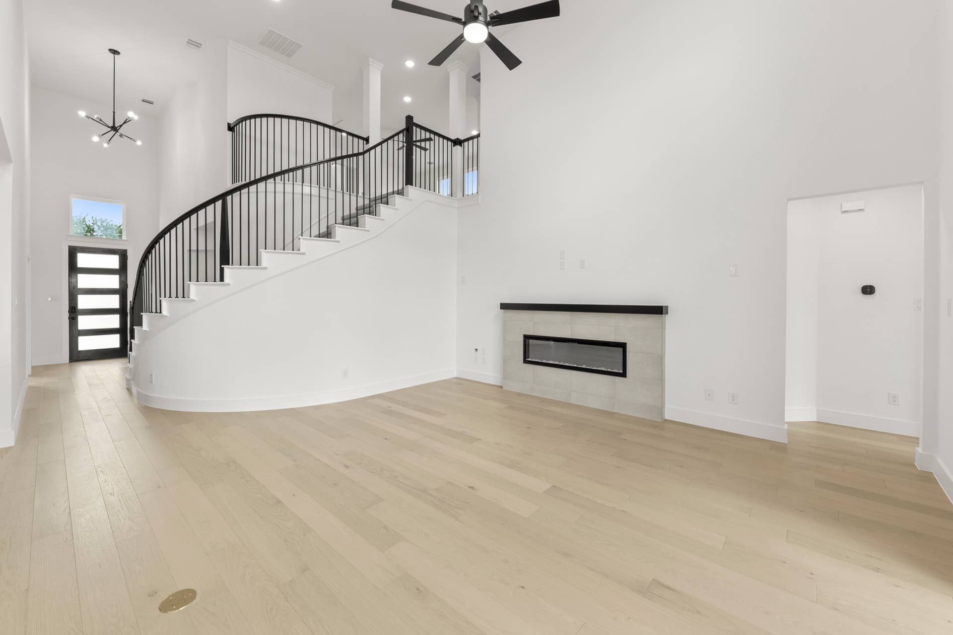 Spacious living room with modern staircase, light wood flooring, and sleek fireplace.