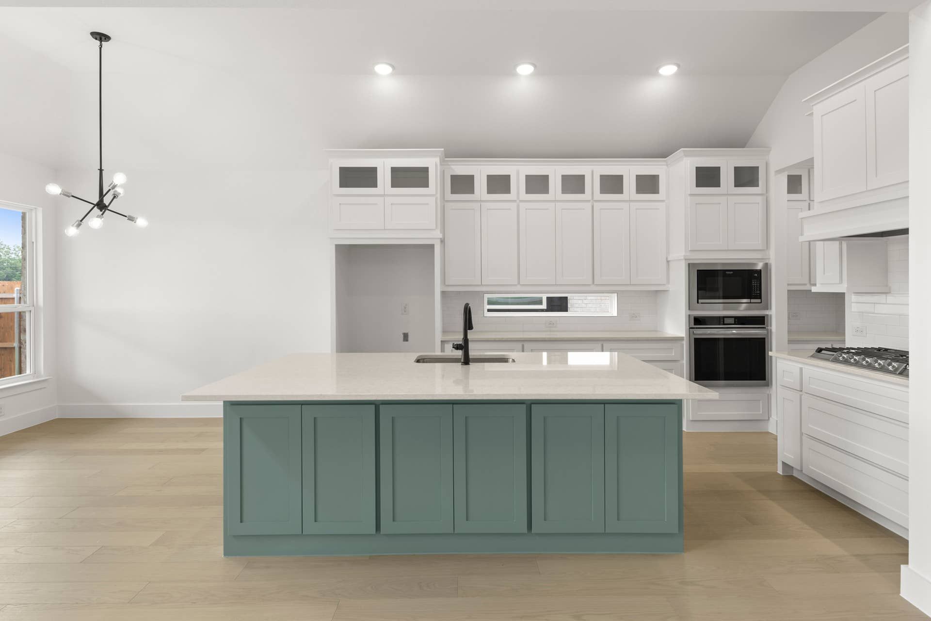 Modern kitchen with teal island, white cabinets, and sleek pendant lighting.