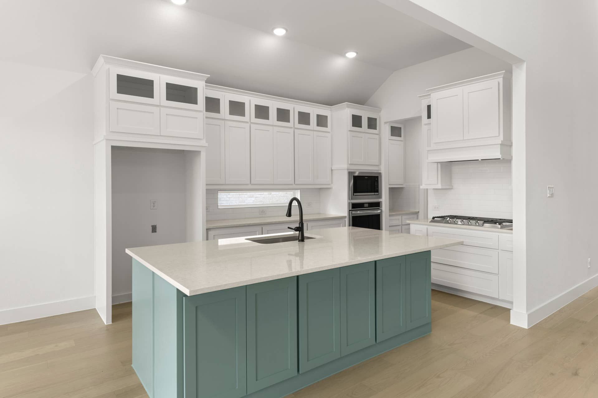 Modern kitchen with teal island, white cabinetry, and stainless steel appliances.