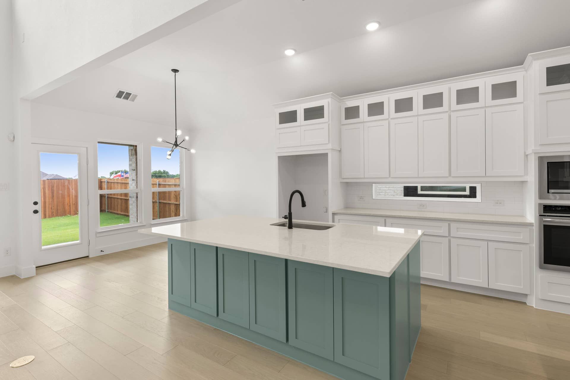 Modern kitchen with teal island, white cabinetry, and pendant lighting.