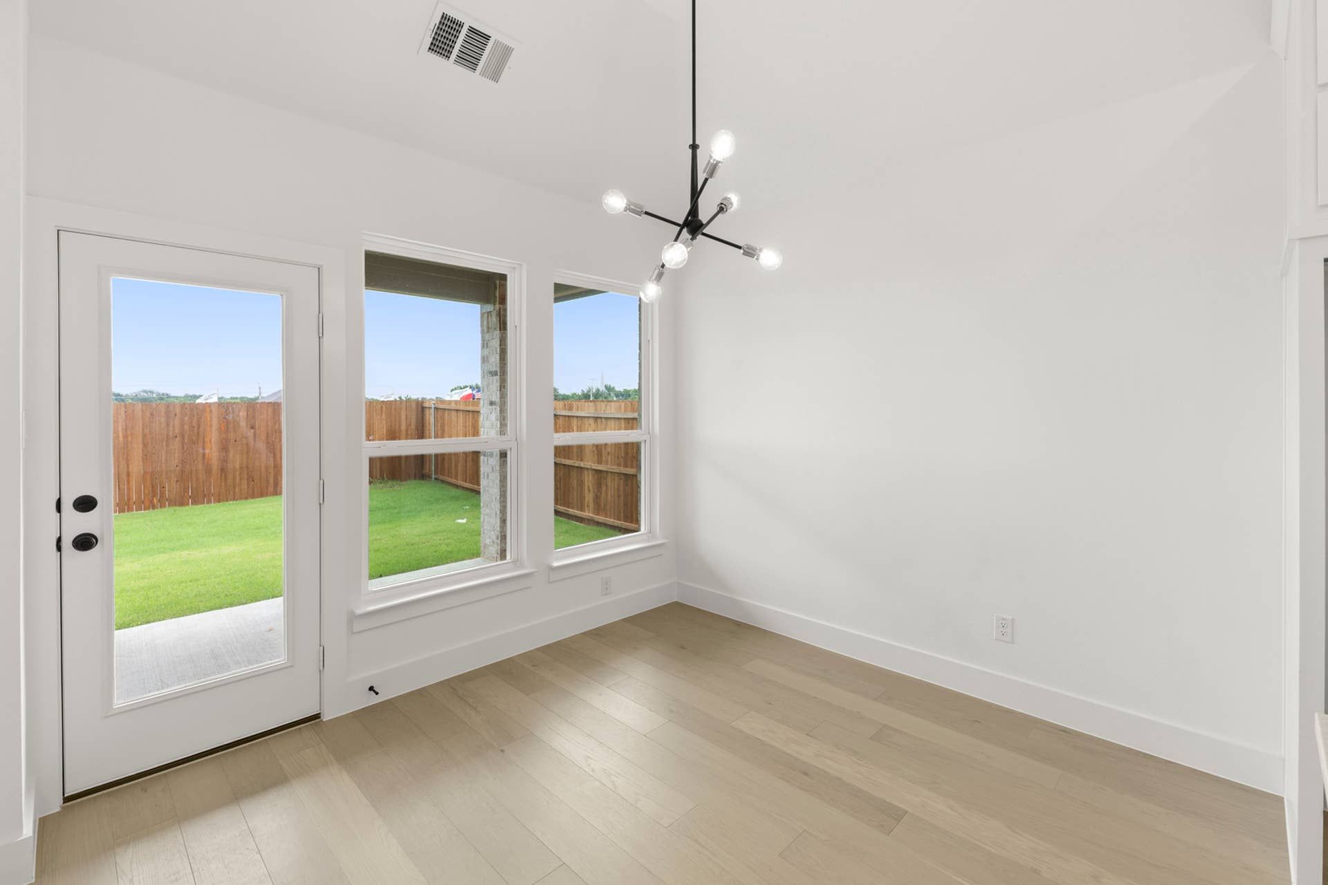 Bright interior nook with modern chandelier and view of fenced backyard.