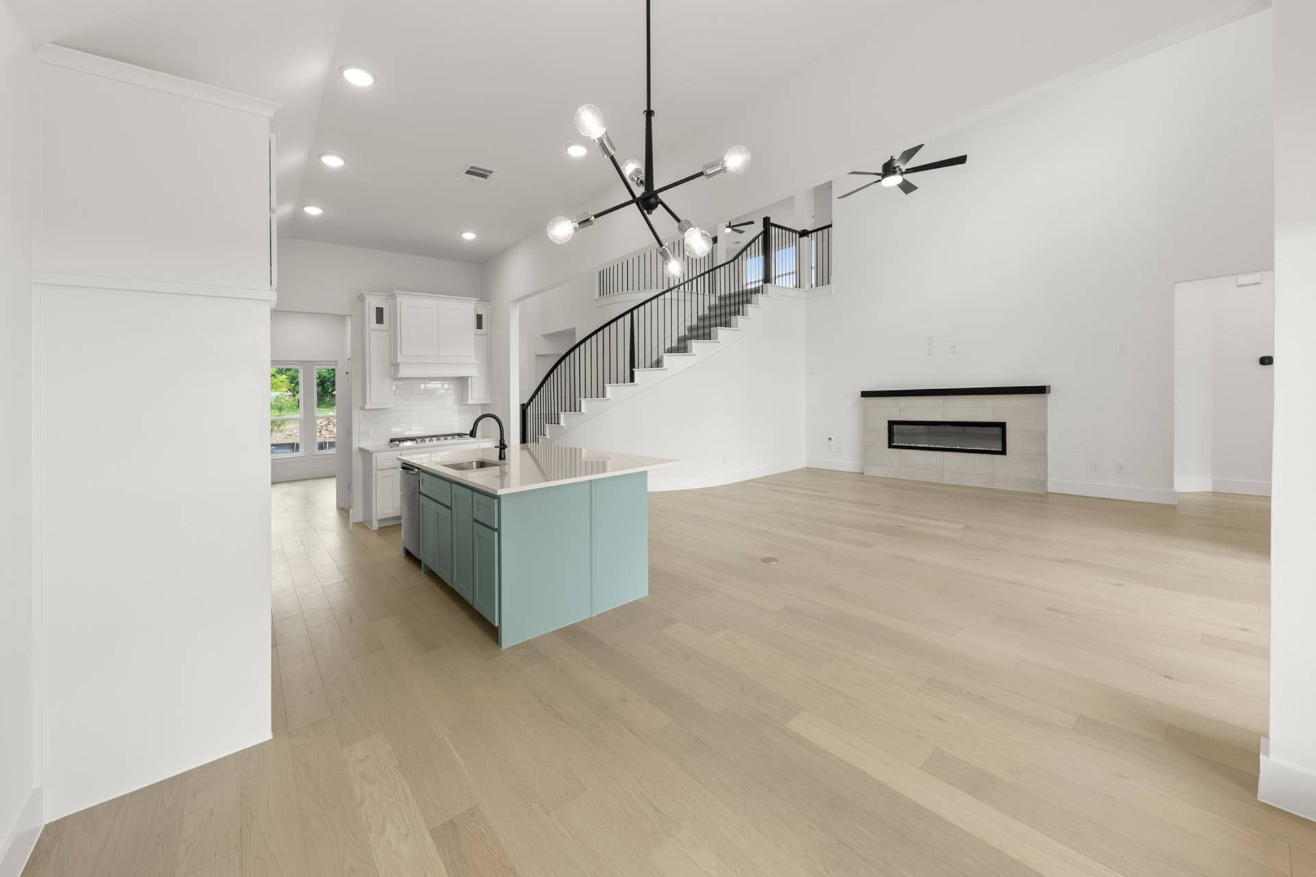 Modern open-concept interior with island kitchen, spiral staircase, and elegant light fixture.
