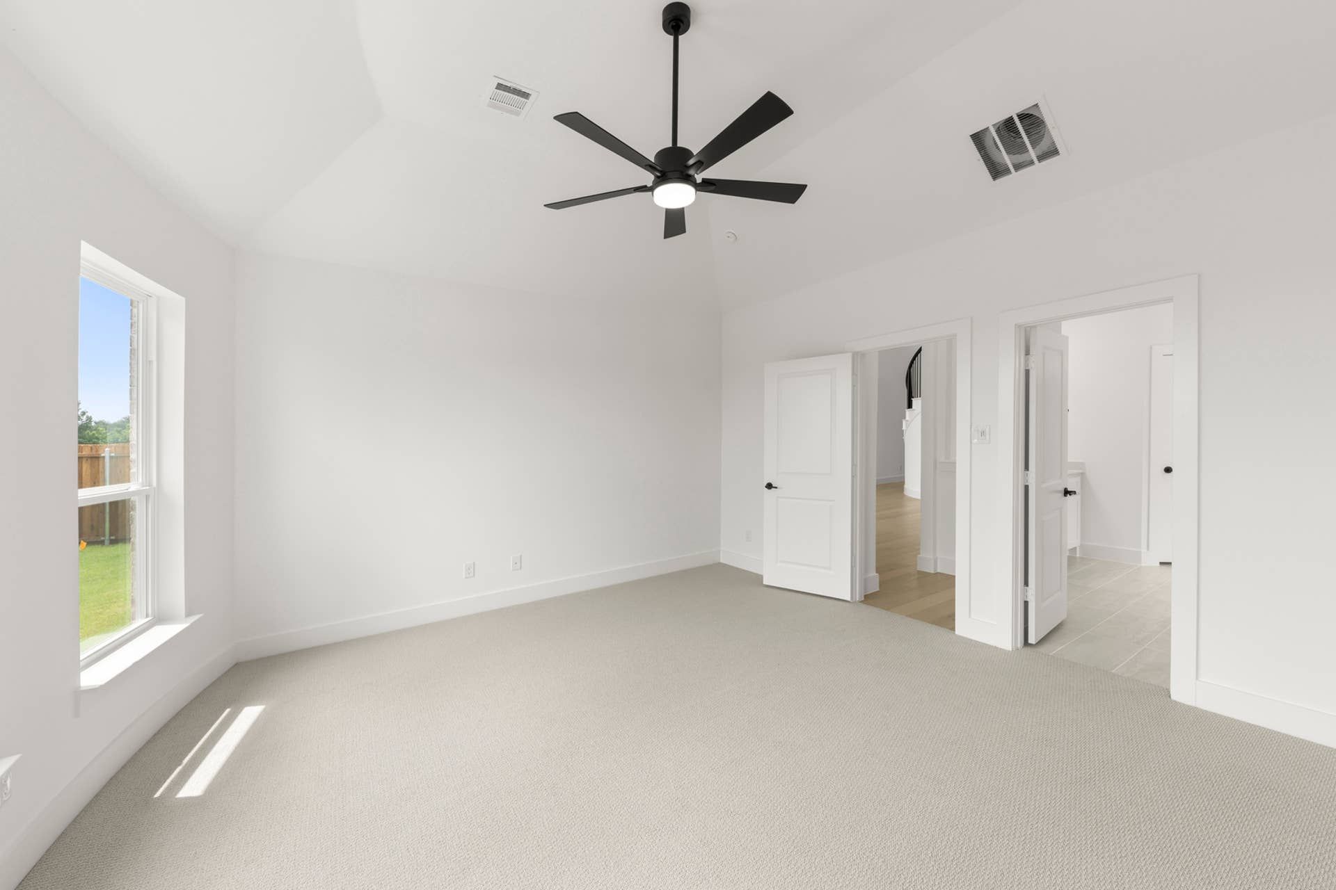 Spacious, bright bedroom with modern ceiling fan and dual white doors.