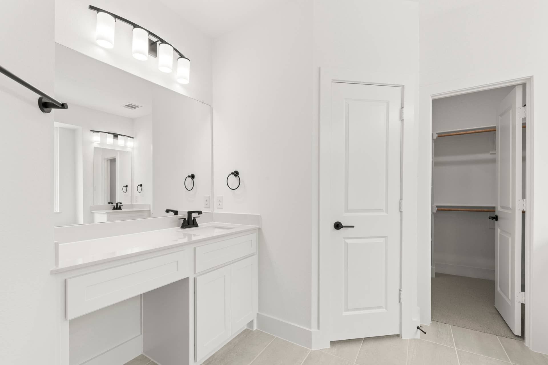 Modern bathroom with white vanity, large mirror, and walk-in closet.