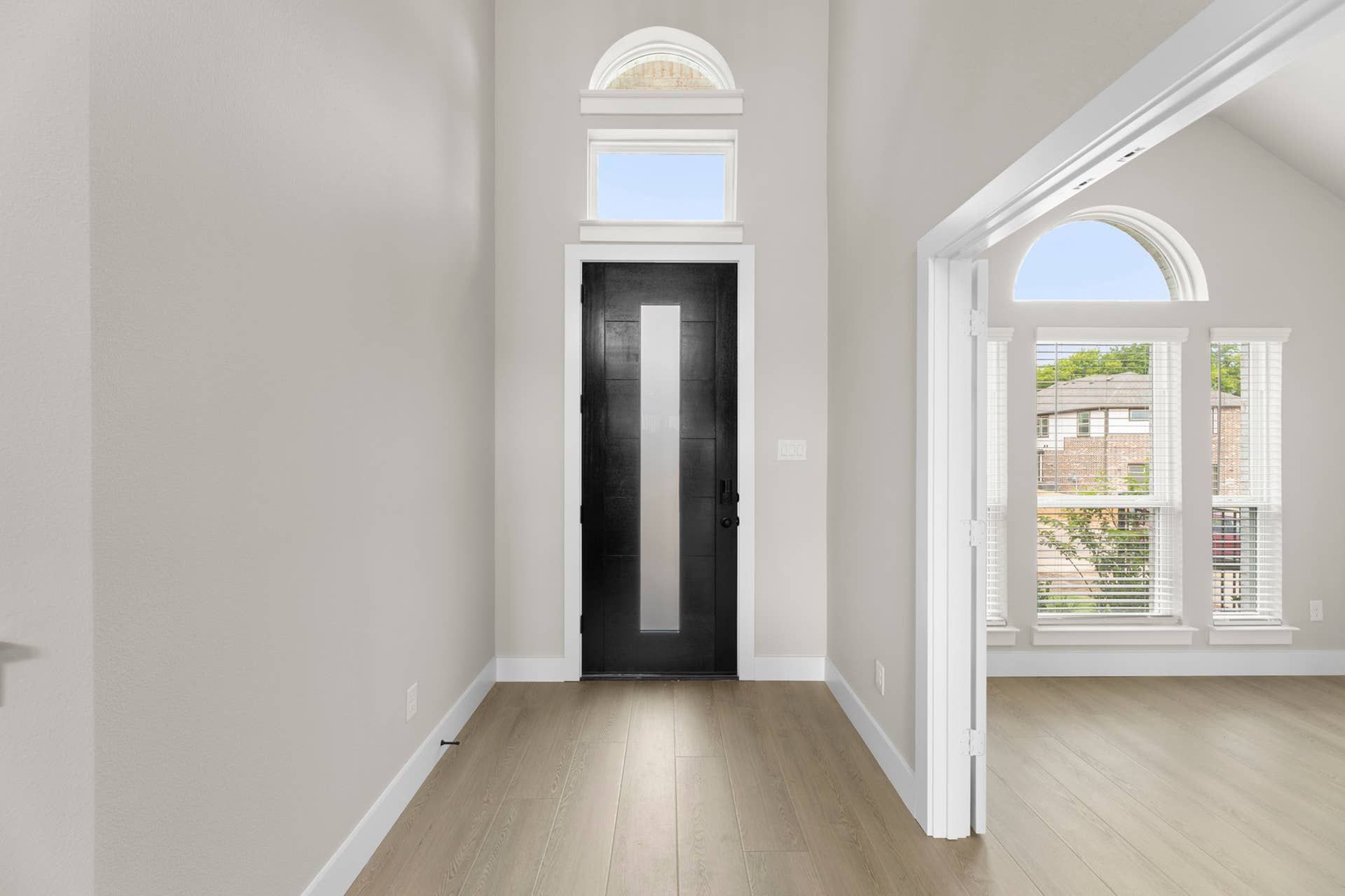 Modern entryway with tall black door and arched window accents.