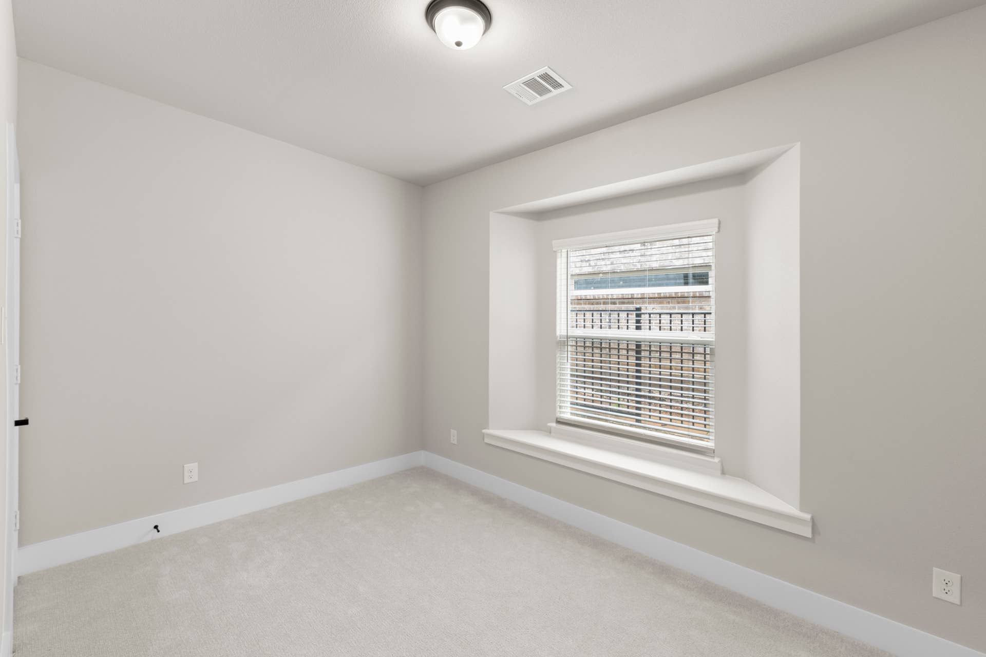 Bright, neutral-toned room with carpet and large window with blinds.