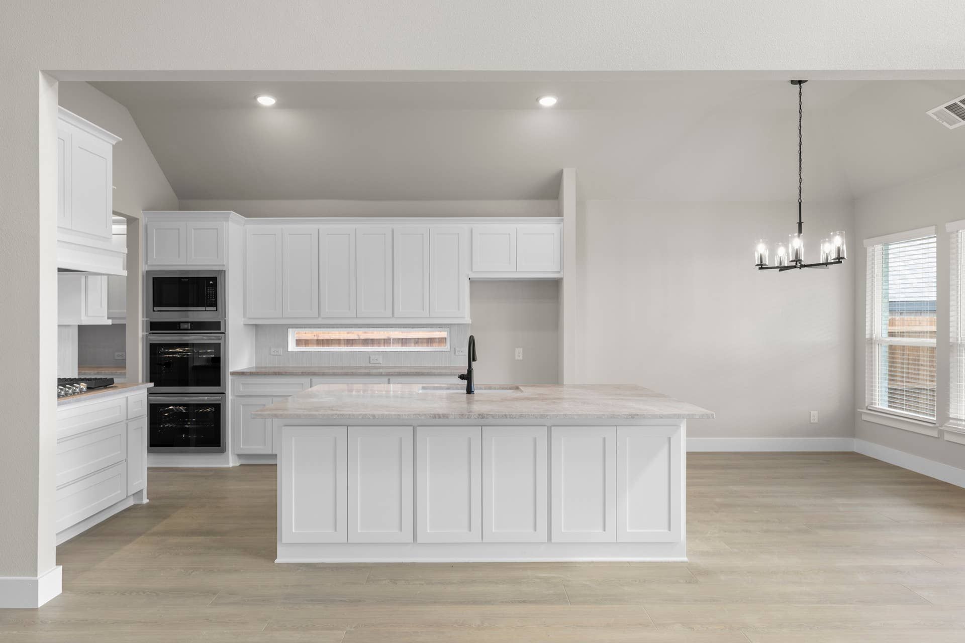 Modern kitchen with white cabinets, island, chandelier, and wood flooring.