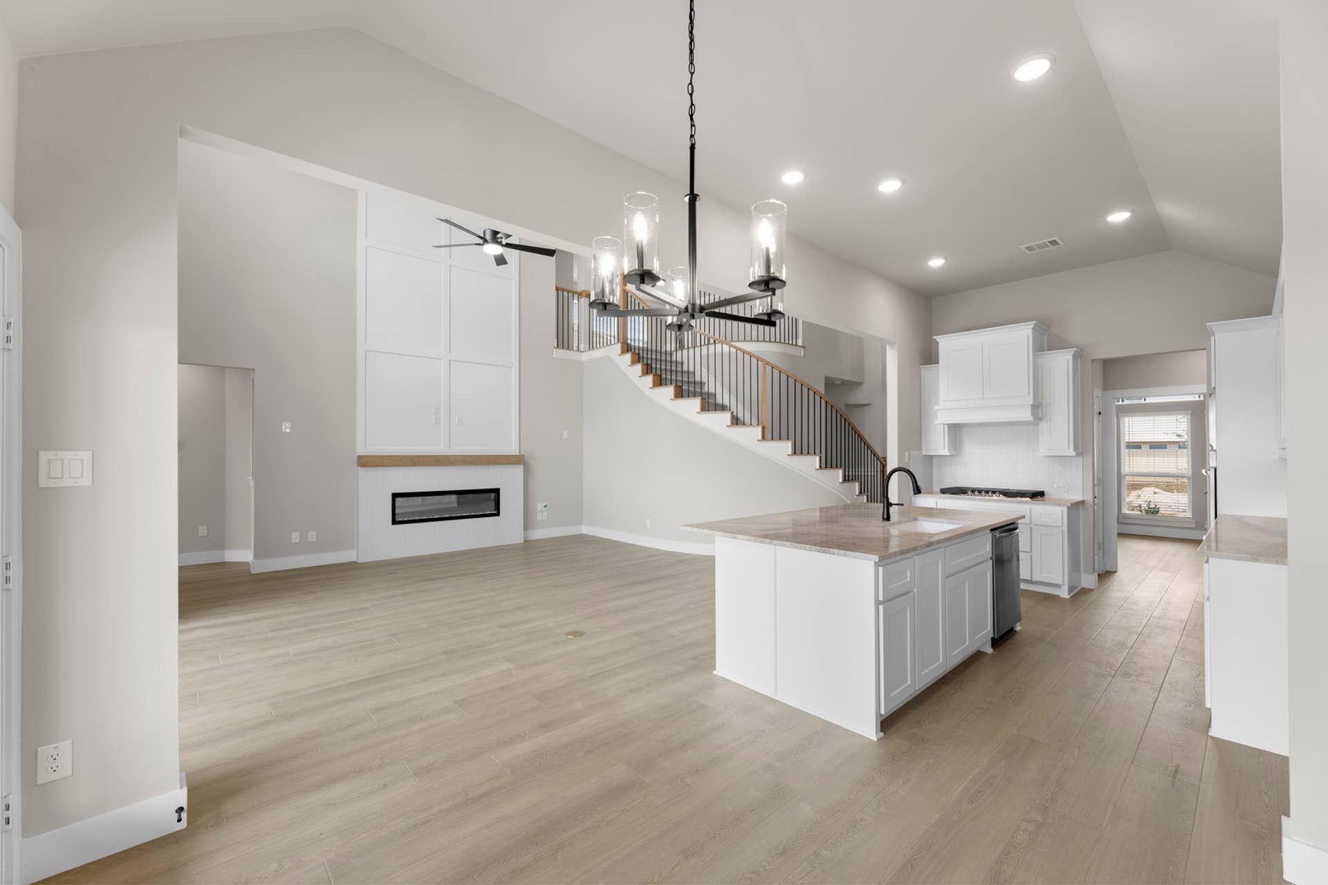 Spacious modern kitchen and living area with staircase and elegant chandelier.