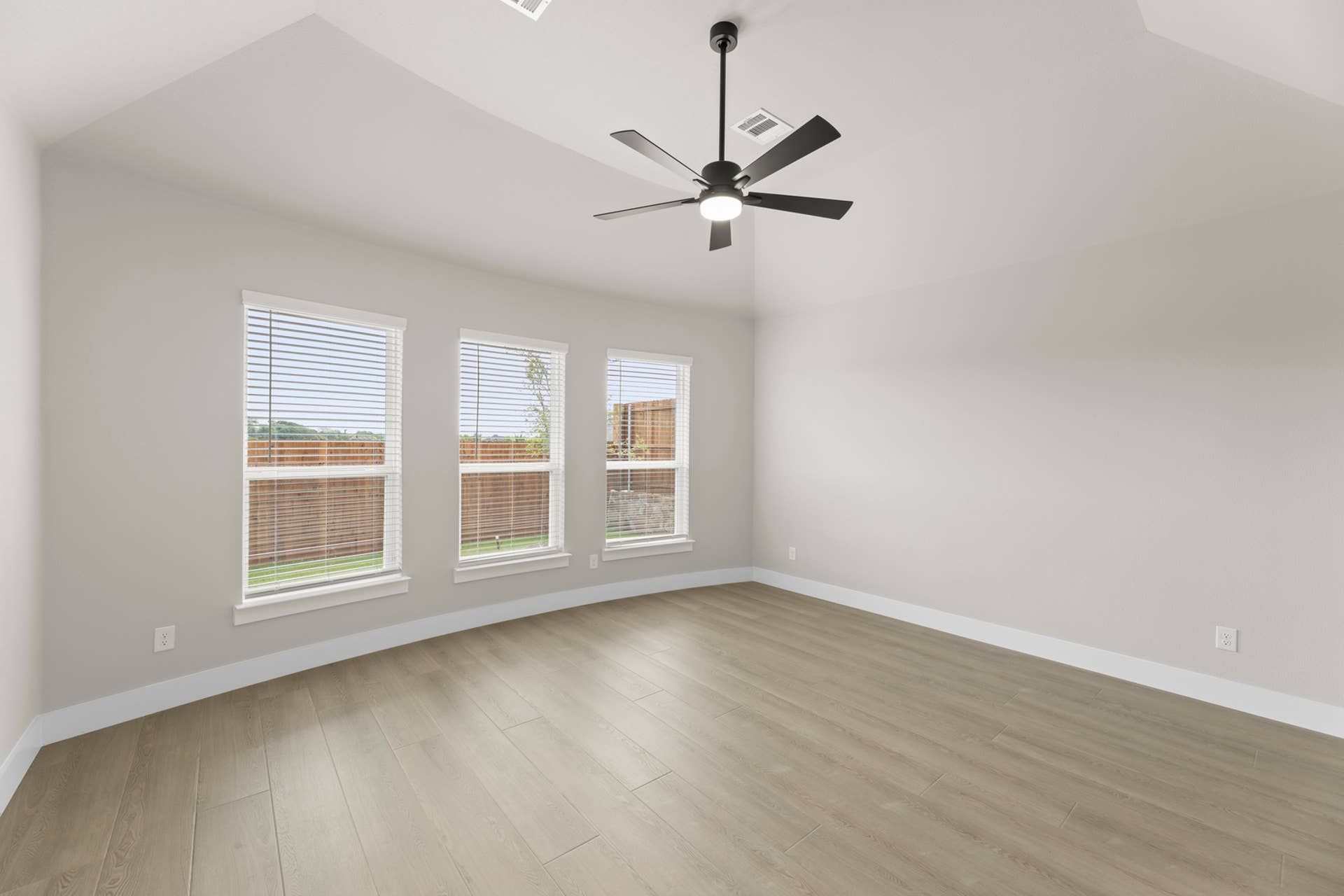 Spacious empty room with hardwood floors, ceiling fan, and large windows.