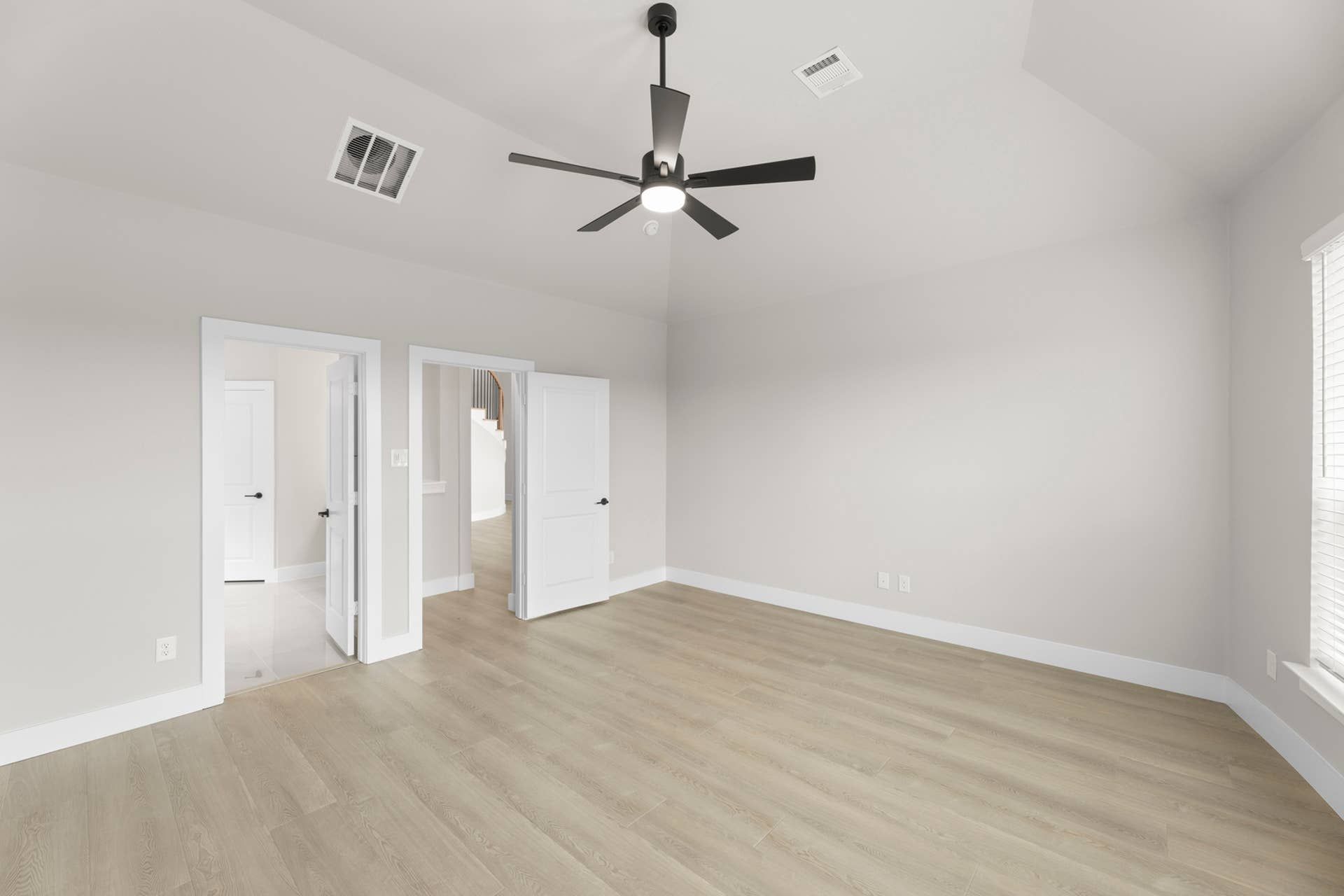 Spacious empty room with light wood flooring and ceiling fan.