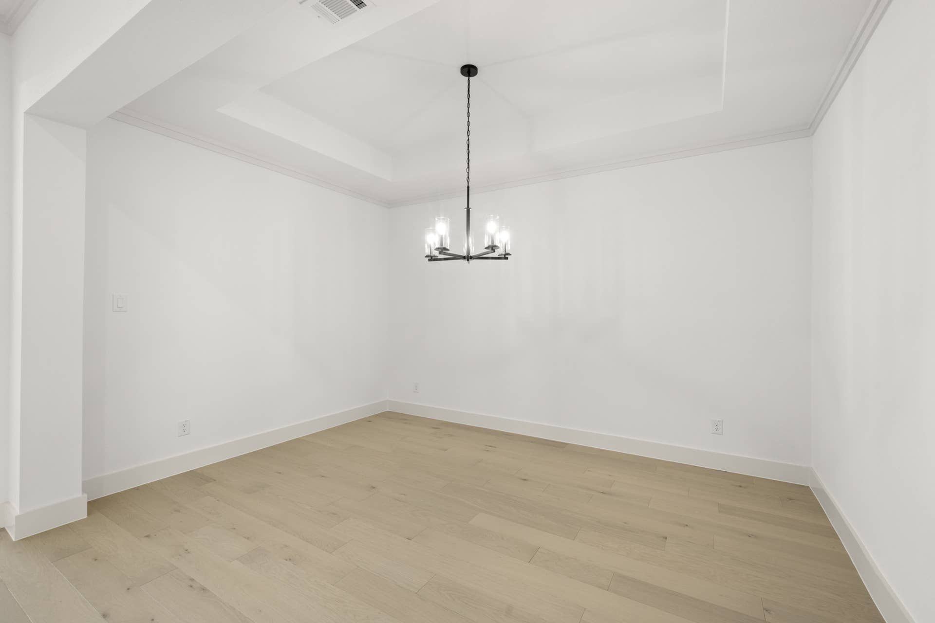 Minimalist dining room with wooden floors and modern chandelier.