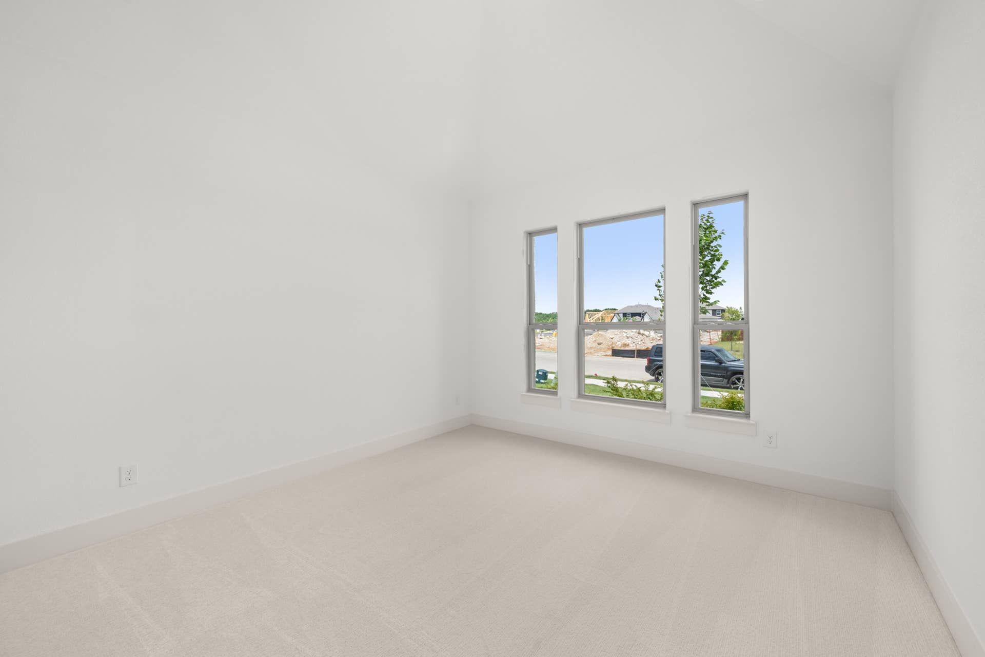 Bright, empty bedroom with large windows and neutral carpeted flooring.