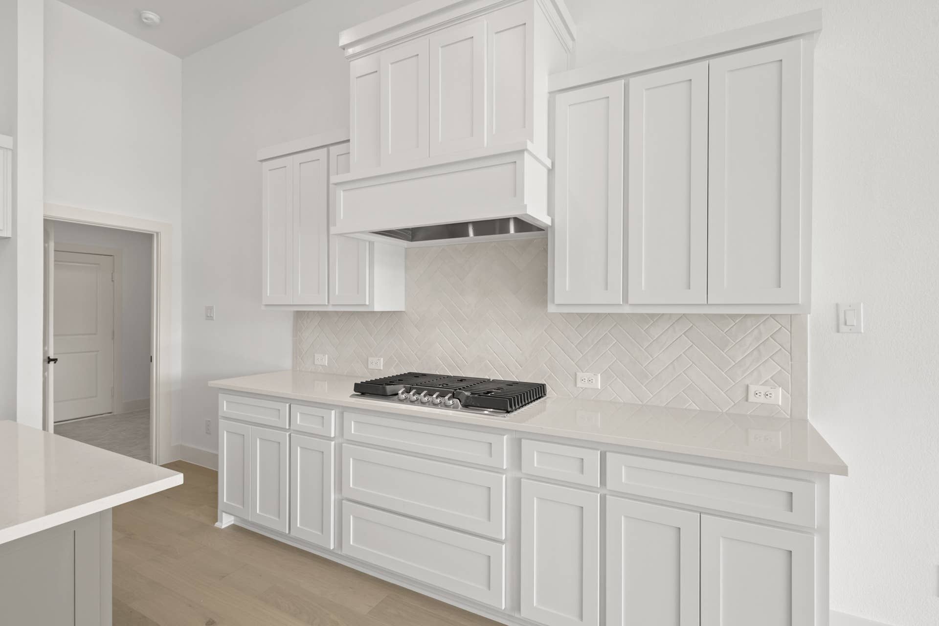 Modern kitchen with white cabinetry and herringbone tile backsplash.