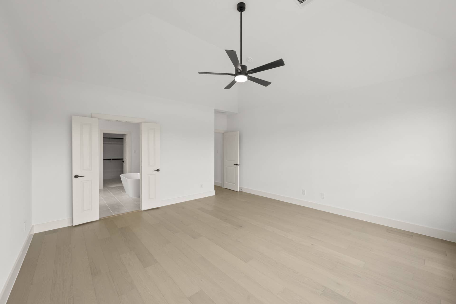 Spacious primary suite with wood flooring and modern ceiling fan.