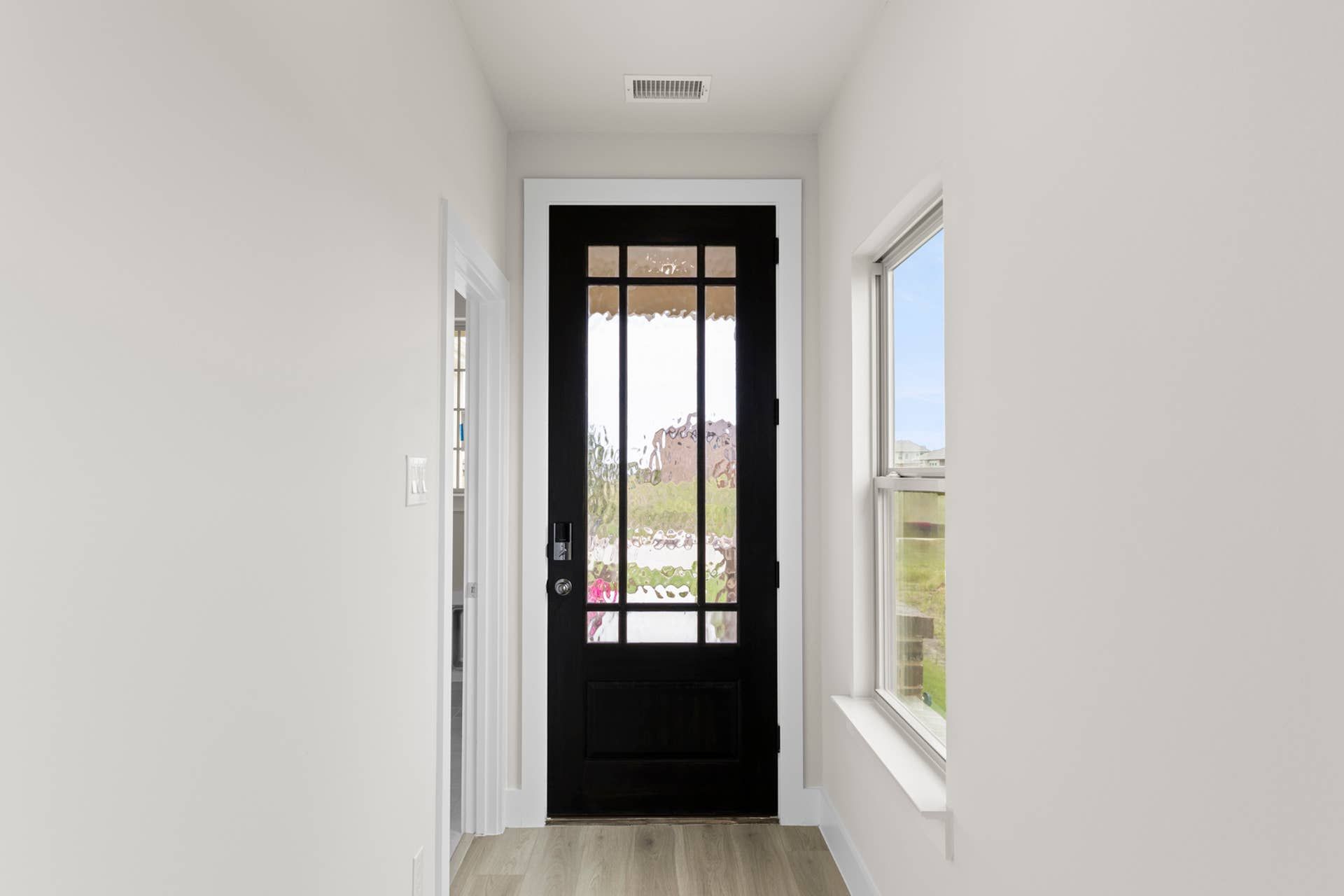 Modern entryway with black framed glass door and light wood flooring.