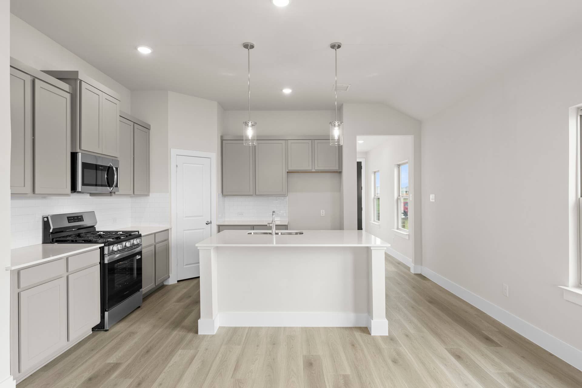 Modern kitchen with white island, gray cabinets, and stainless steel appliances.