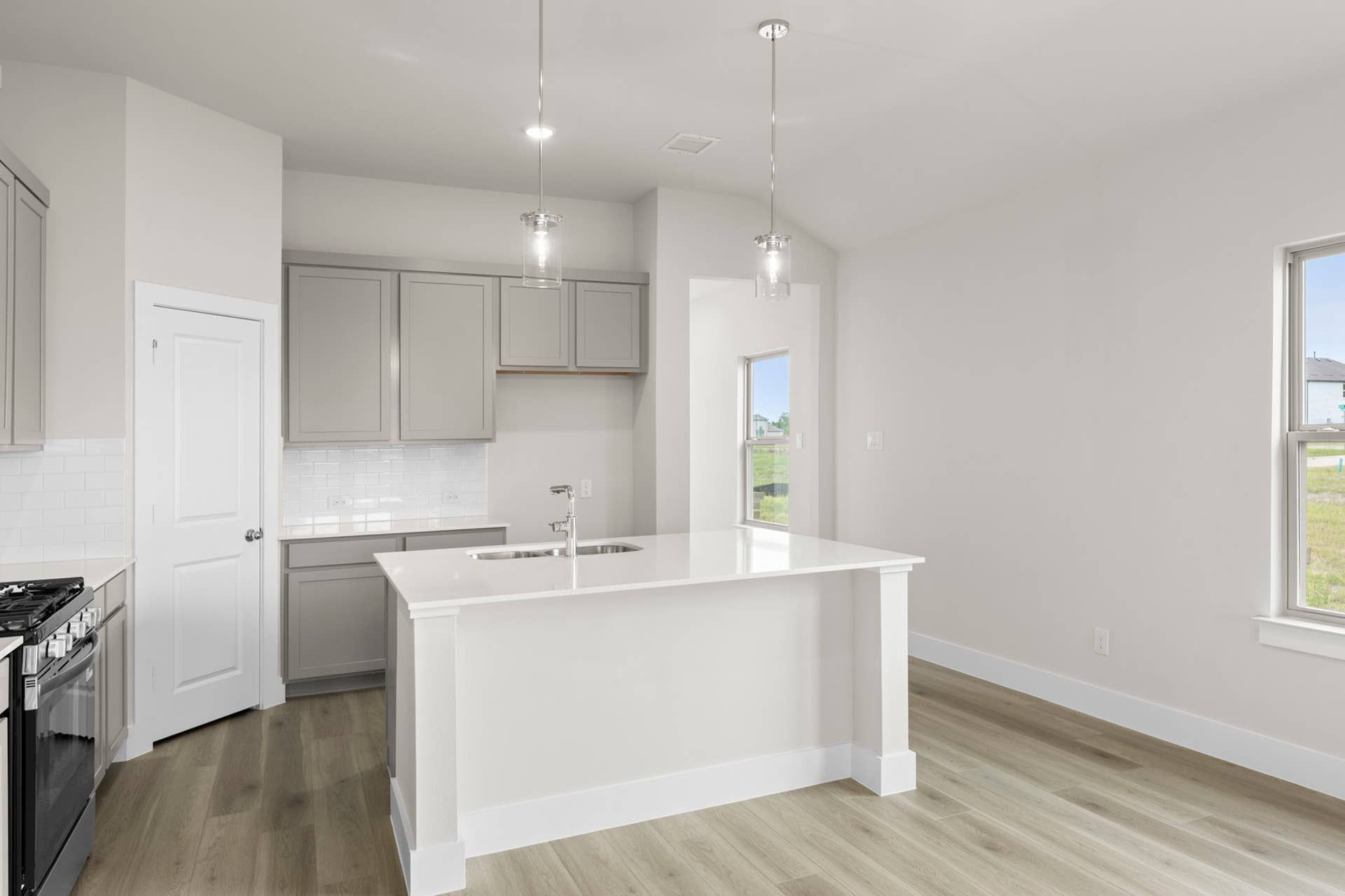 Modern kitchen interior with white island, light wood flooring, and pendant lighting.