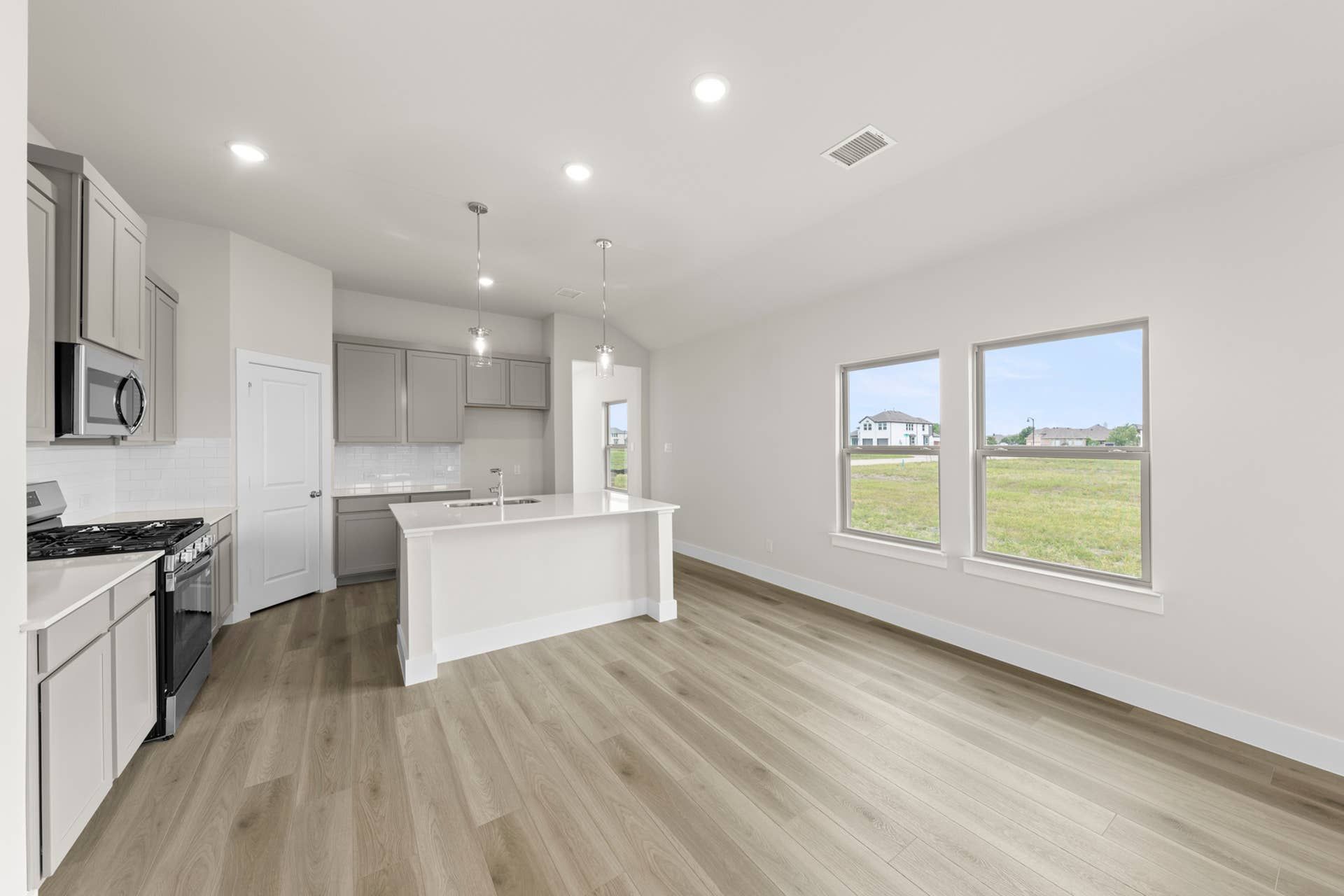 Modern kitchen with island, light wood floors, and large windows overlooking backyard.