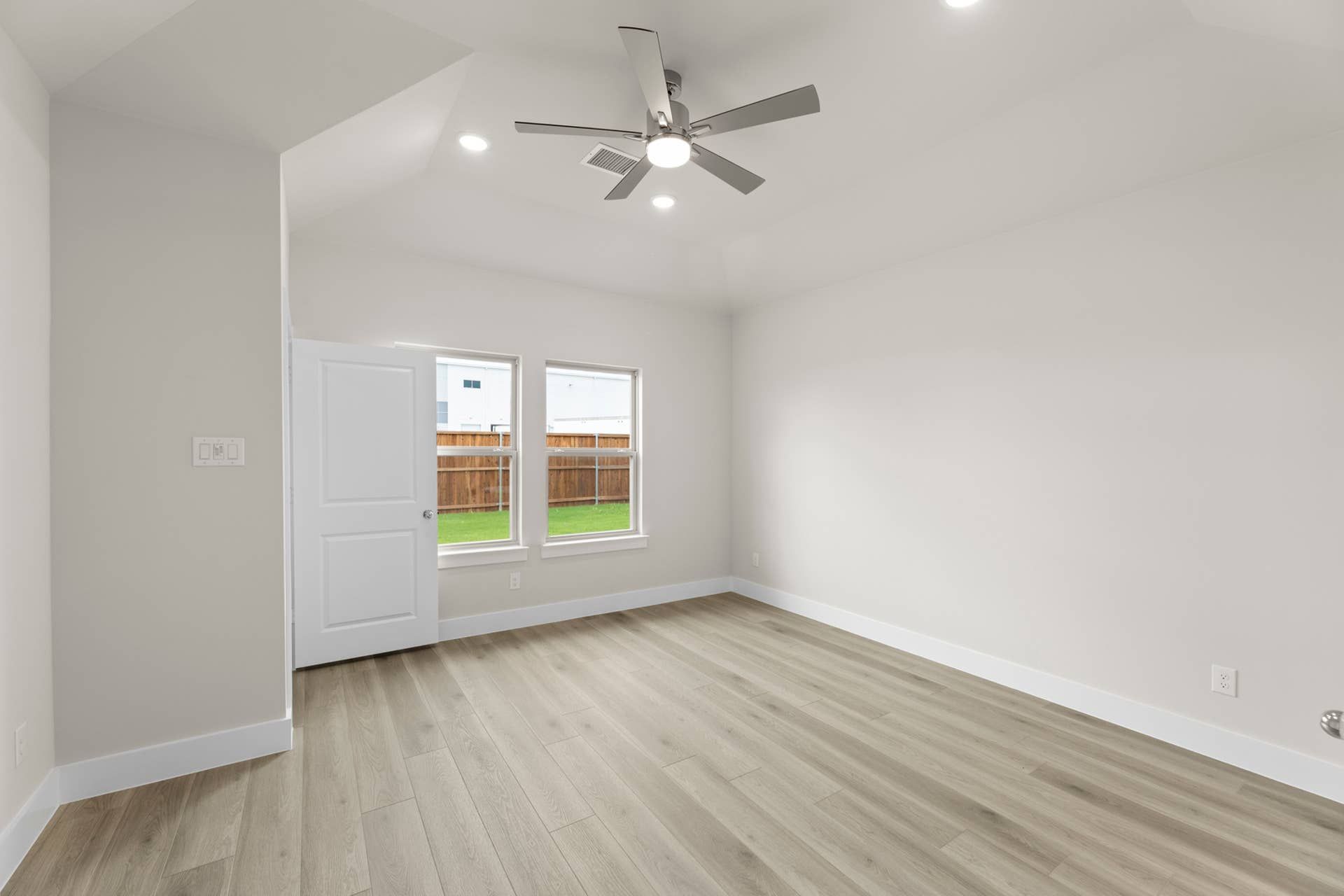 Spacious interior room with wooden floors and ceiling fan, natural light from windows.