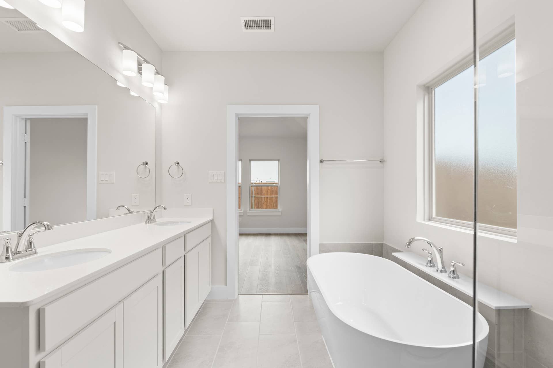 Modern bathroom with double vanity, freestanding tub, and large window.