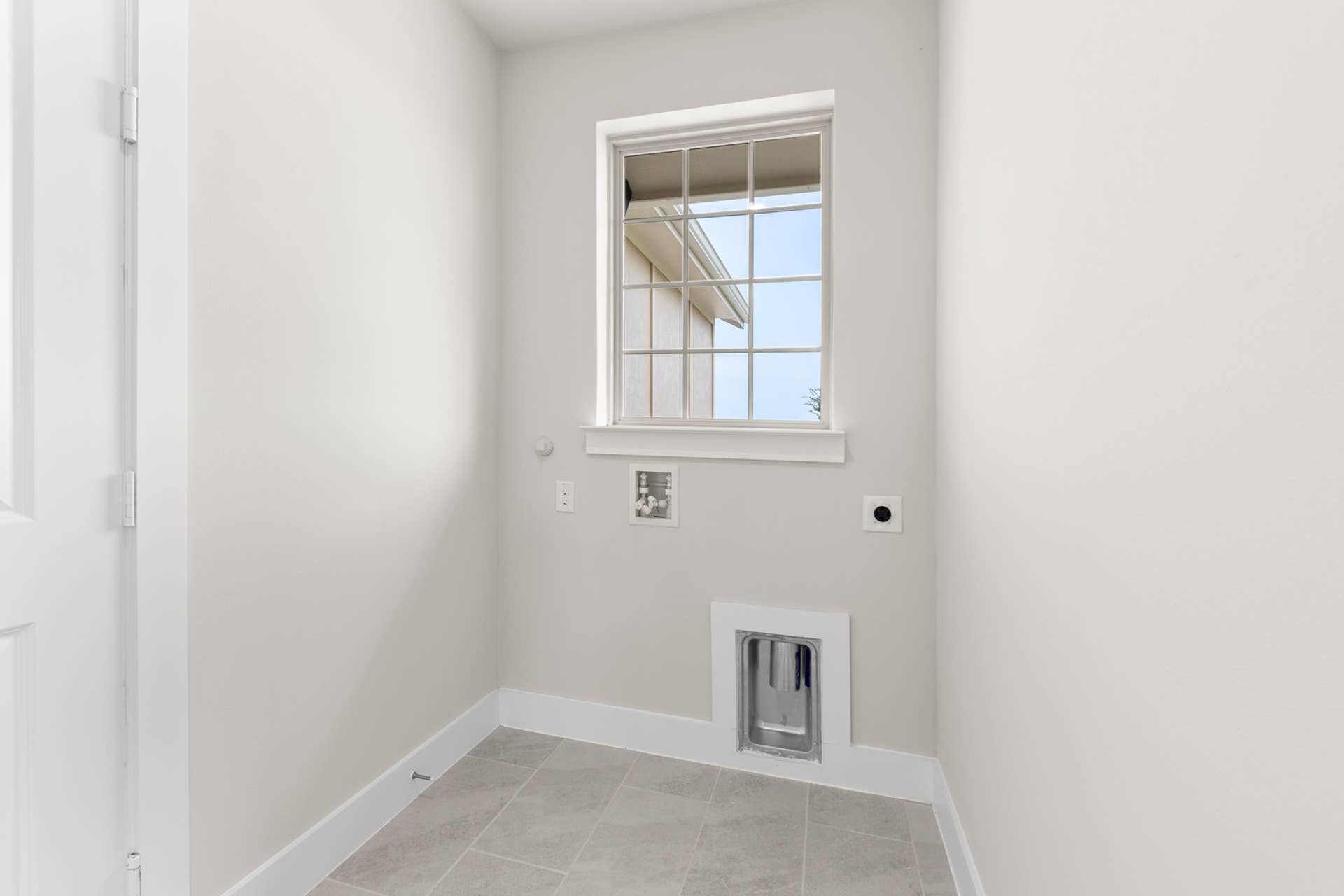Utility room with window, plumbing and electrical hookups, and tile flooring.