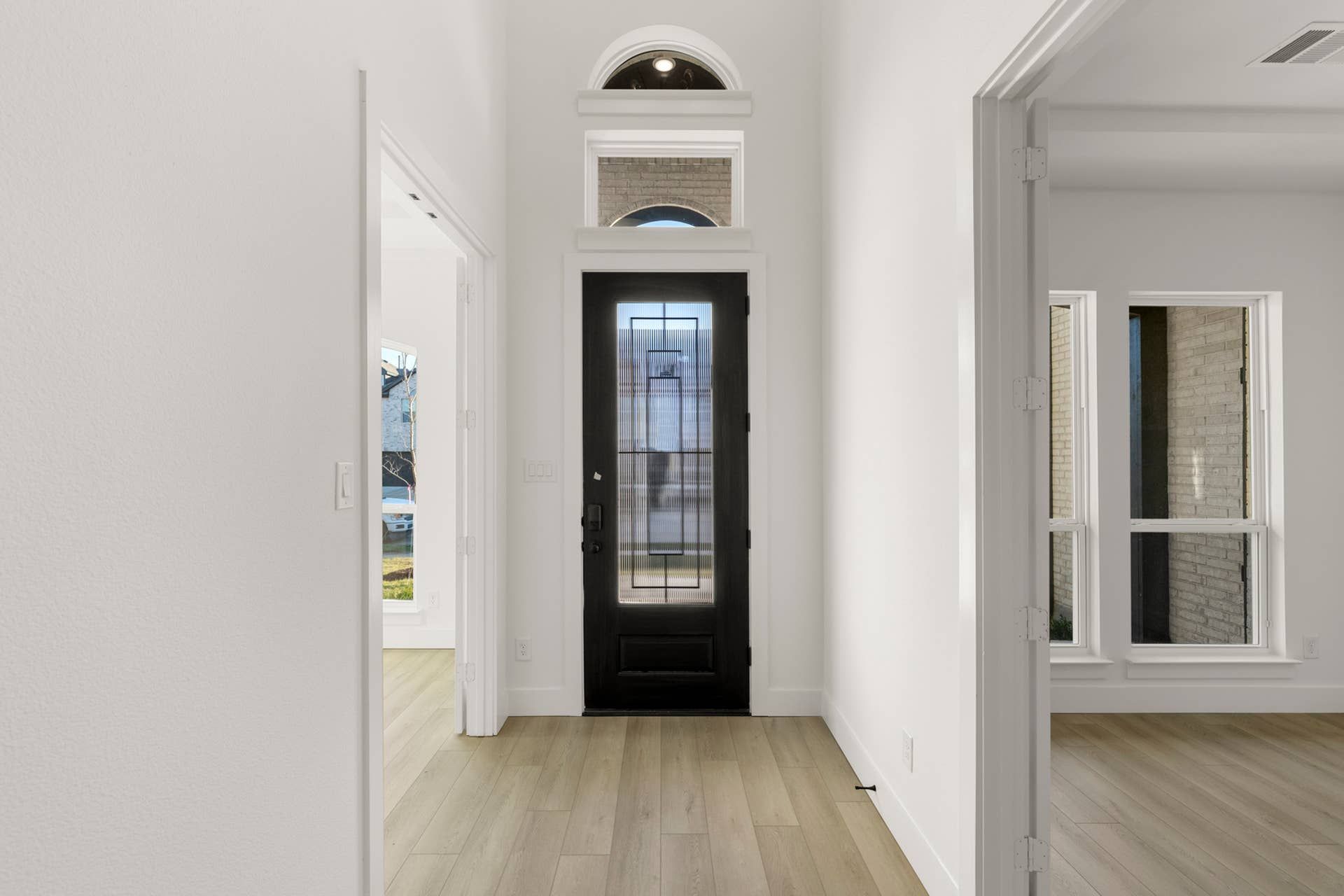 Bright entryway with black door and wood flooring, featuring transom windows.