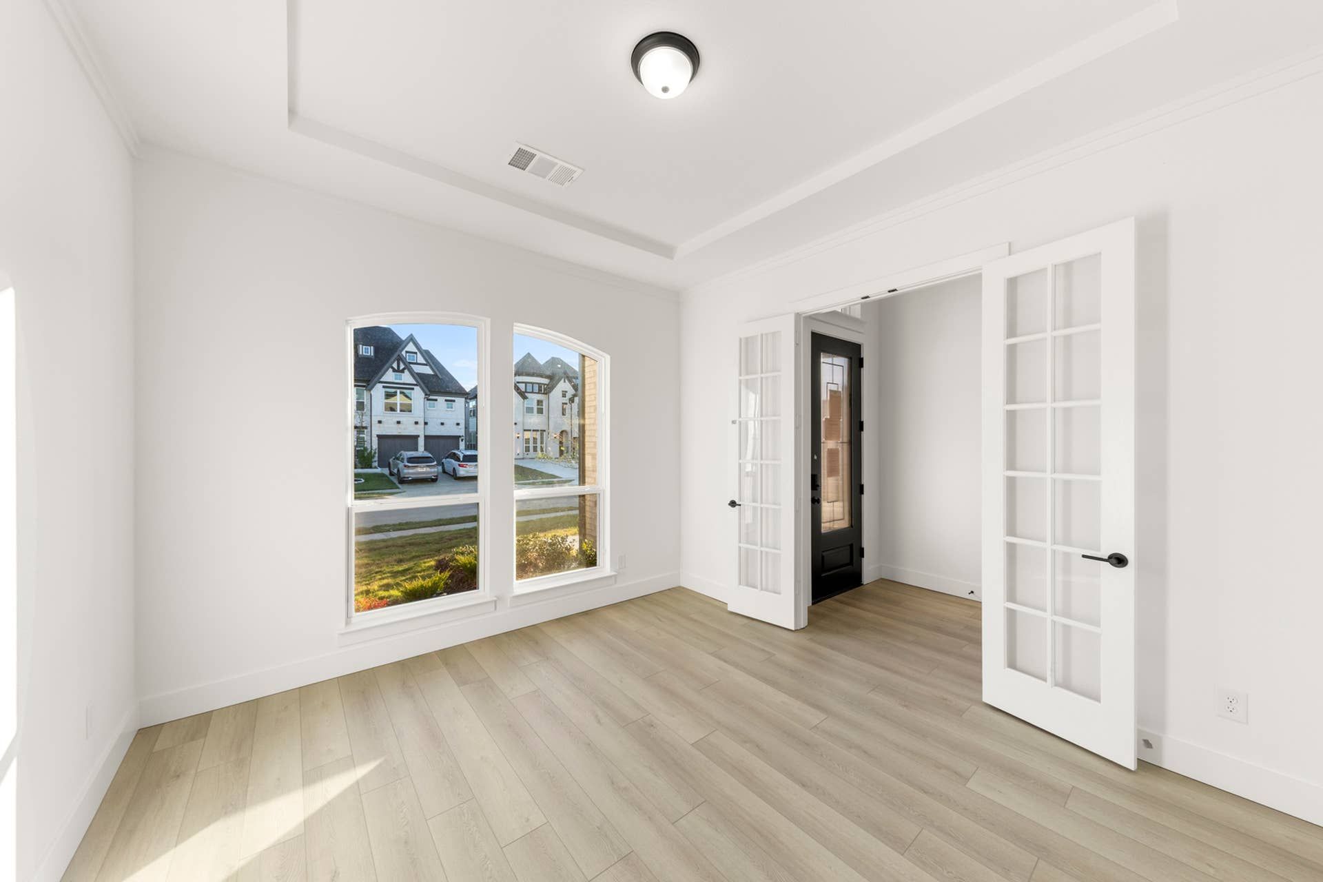 Bright study room with French doors and large windows overlooking neighborhood.