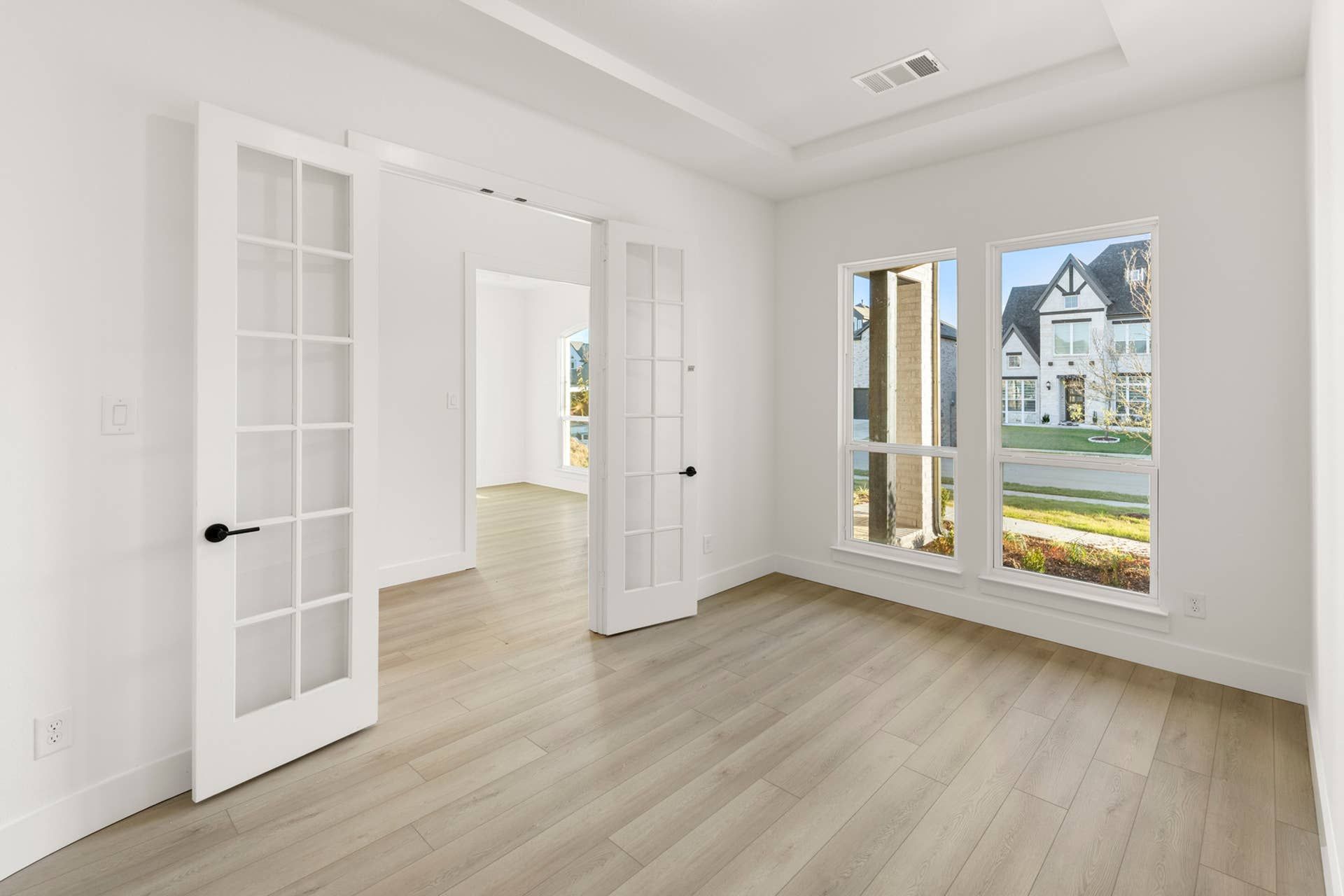 Bright room with French doors, hardwood floors, and large windows overlooking a suburban street.