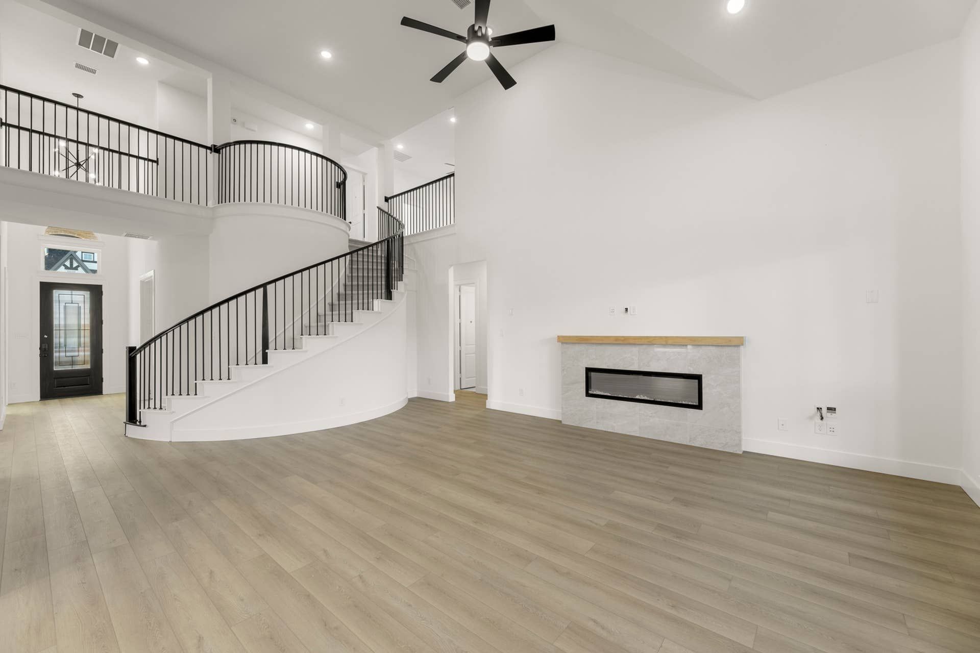 Spacious living room with curved staircase, modern fireplace, and high ceiling.