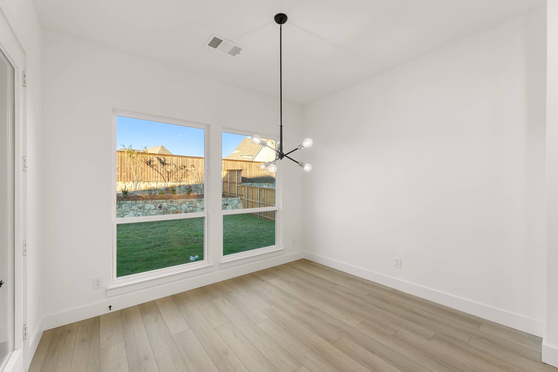 Bright dining nook with modern chandelier and large windows overlooking backyard.