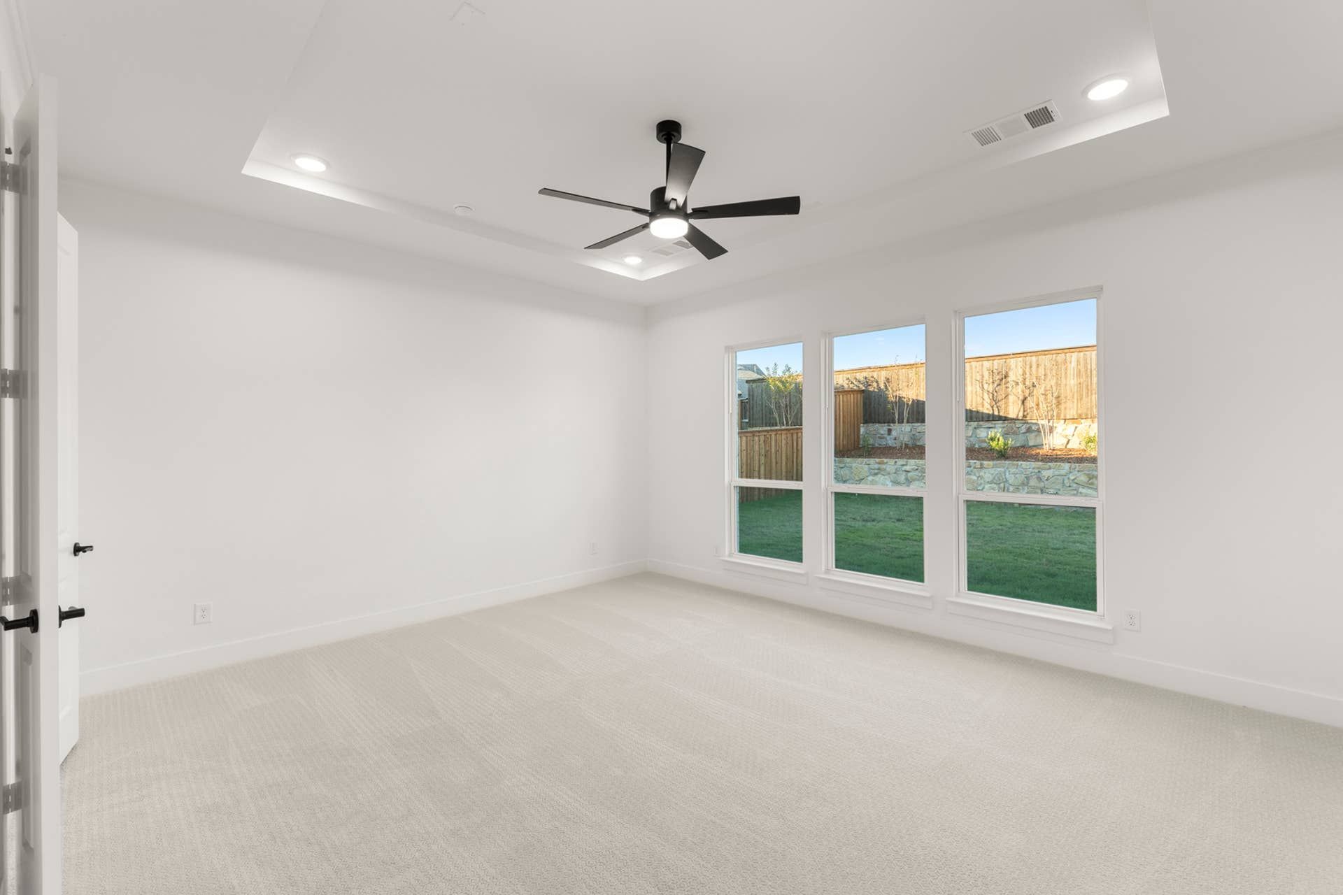 Spacious room with large windows, tray ceiling, and modern ceiling fan.