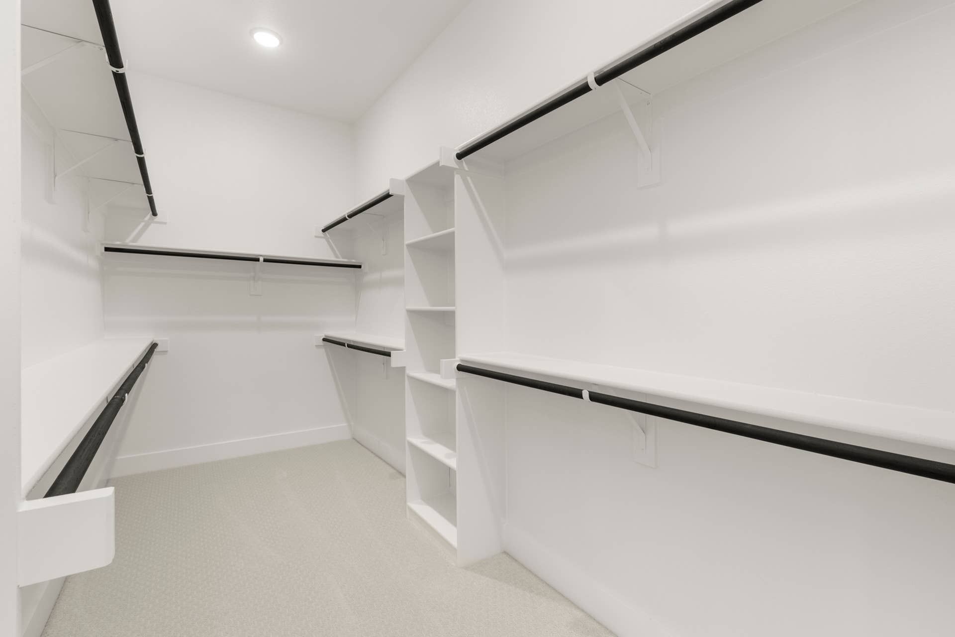 Spacious walk-in closet with white shelving and black hanging rods.