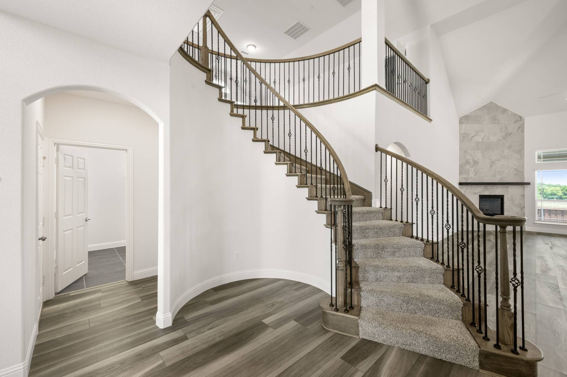 Curved staircase with wrought iron railing and wood flooring in modern interior.
