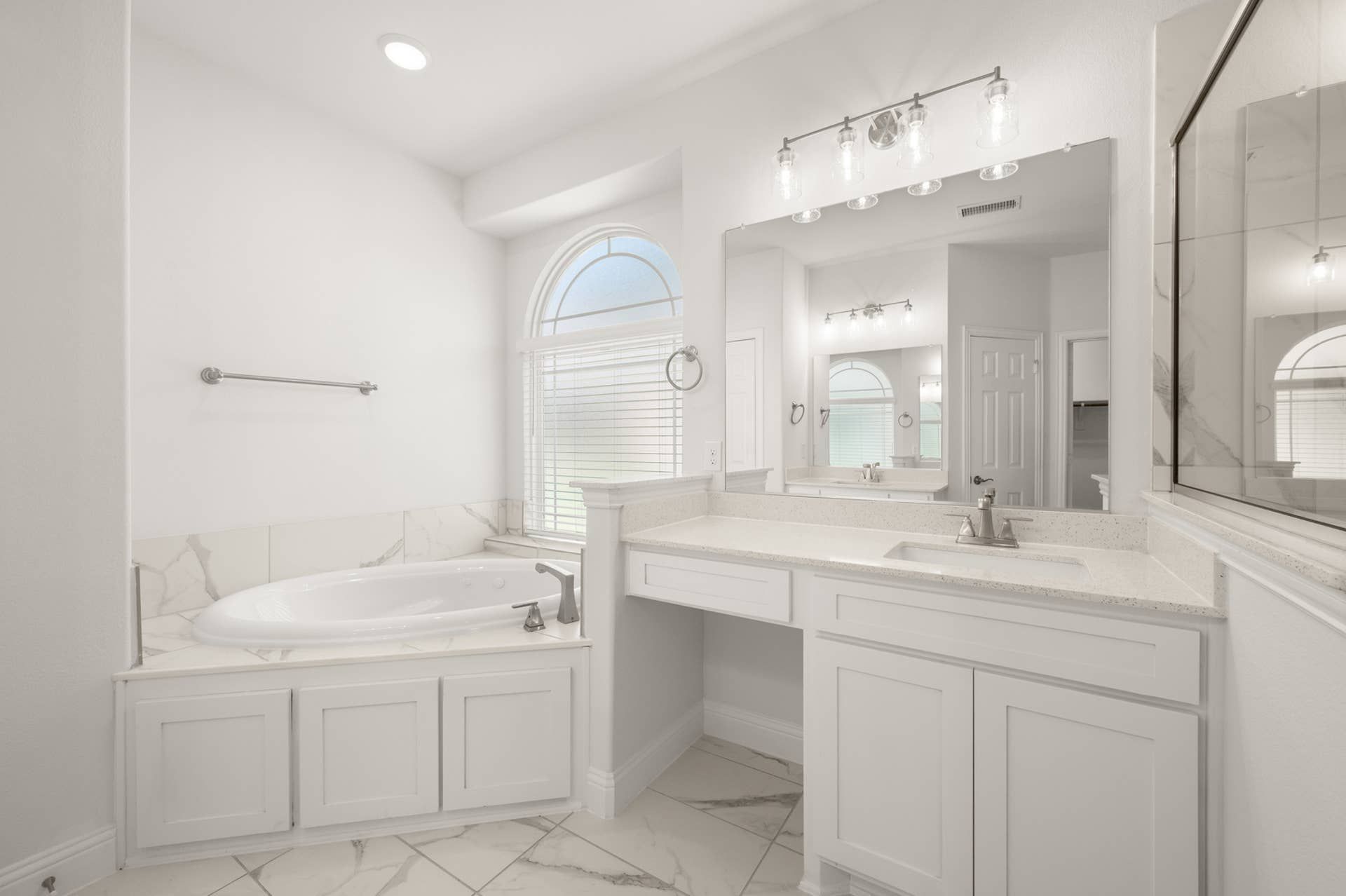 Luxurious primary bathroom with soaking tub, large vanity, and elegant arched window.