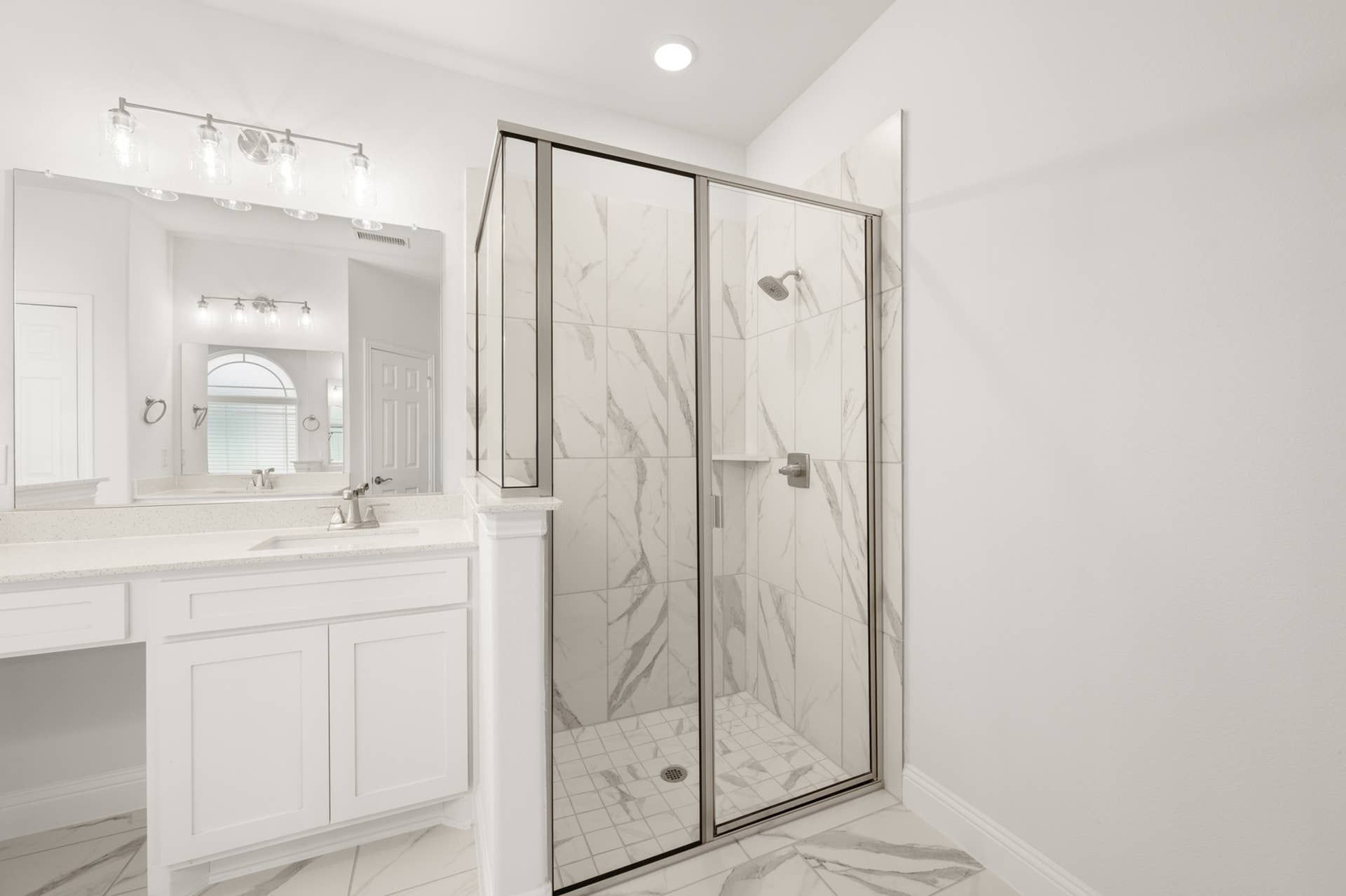 Elegant primary suite bathroom with marble shower and modern vanity lighting.