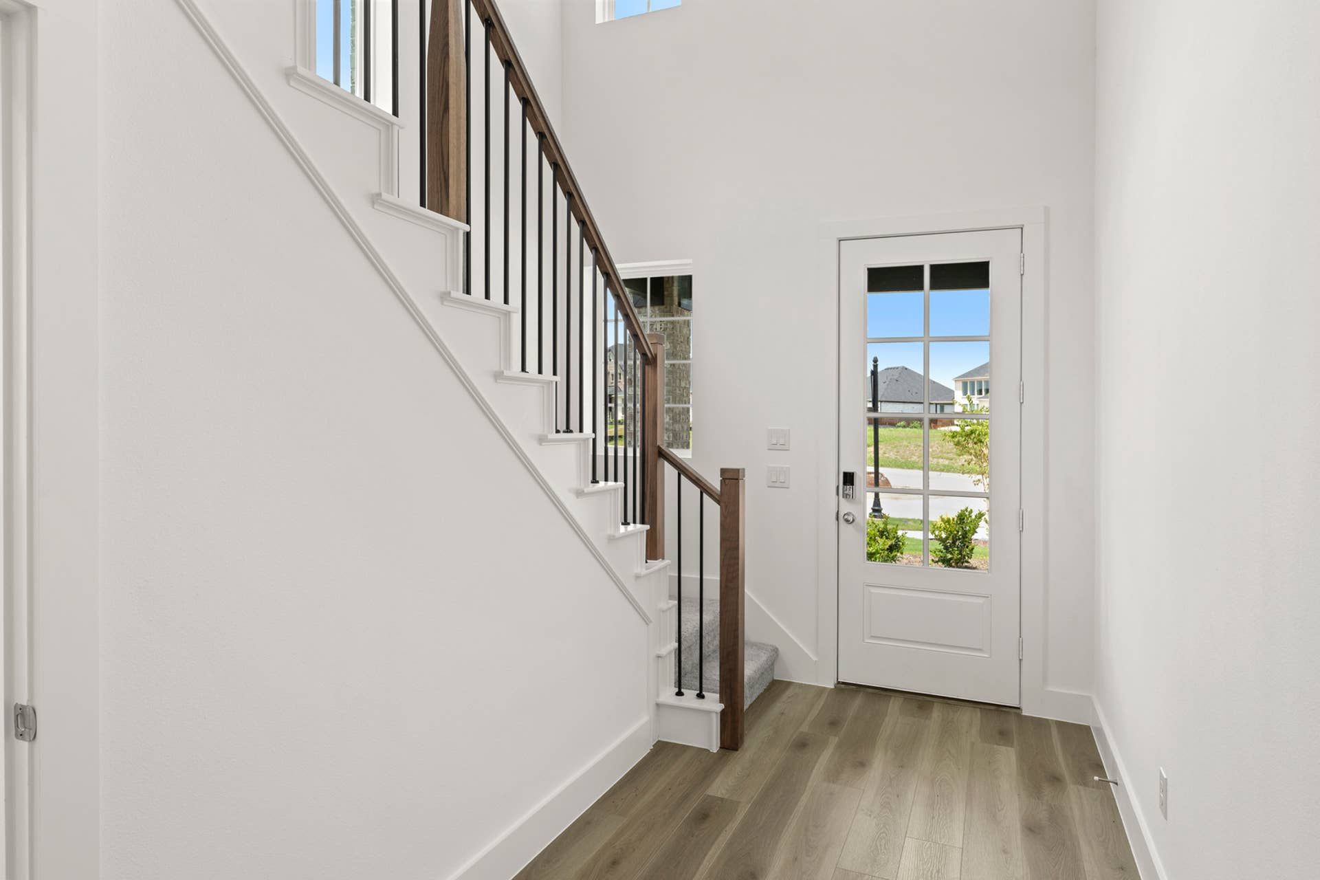 Bright entryway with modern staircase and glass-paneled front door.