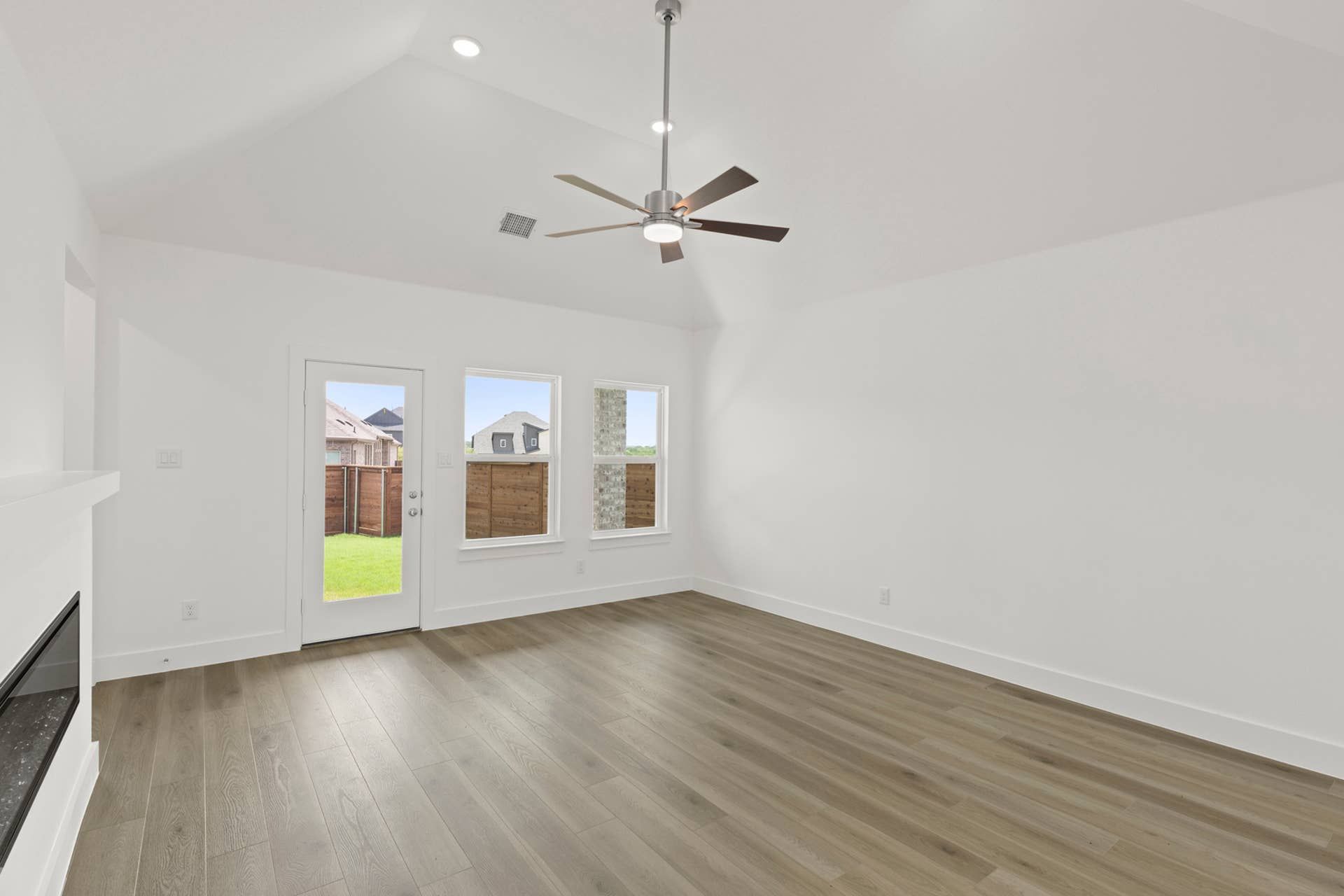Spacious family room with hardwood floors, ceiling fan, and backyard view.