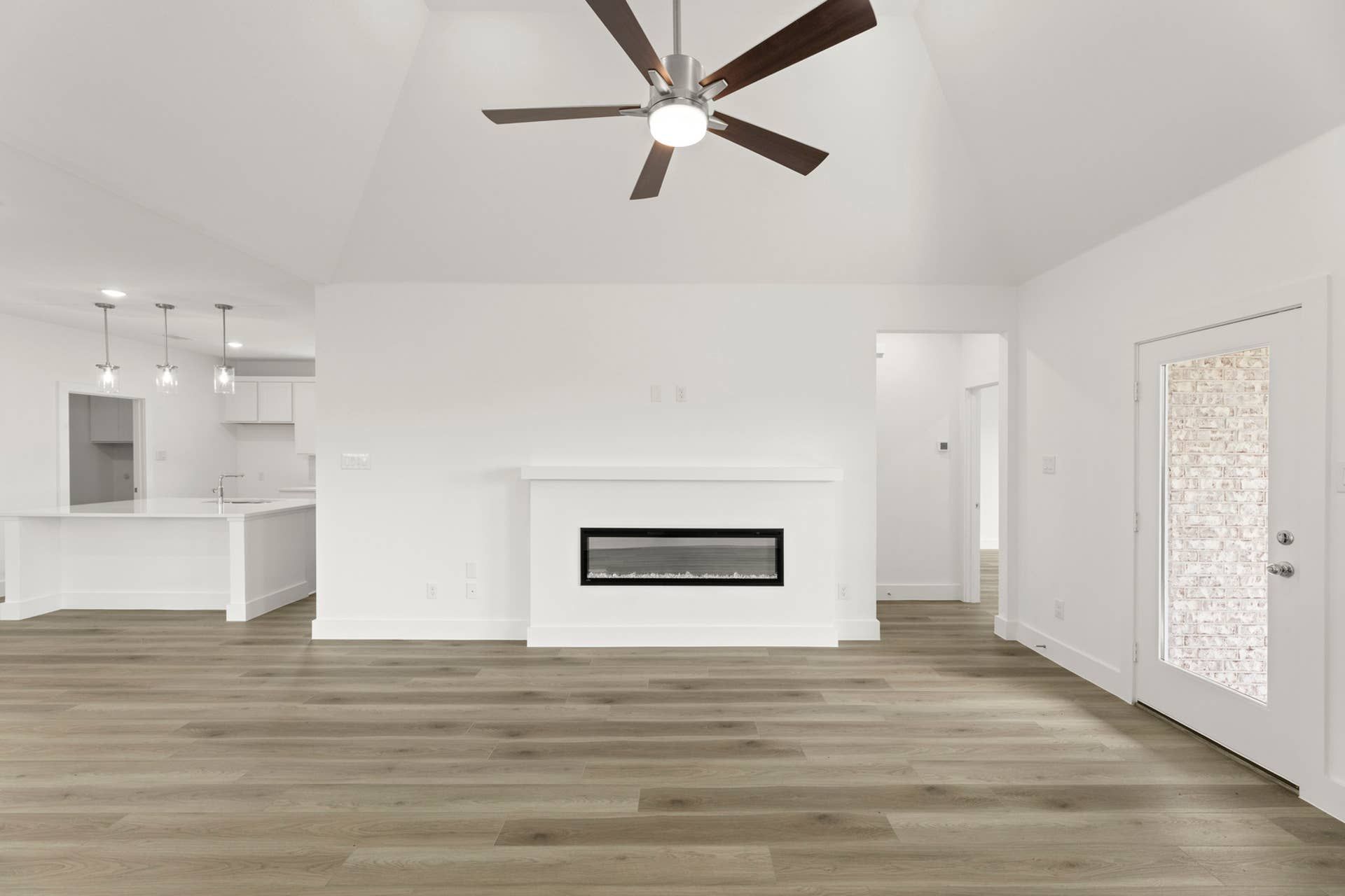Modern living room with ceiling fan, sleek fireplace, and open kitchen area.