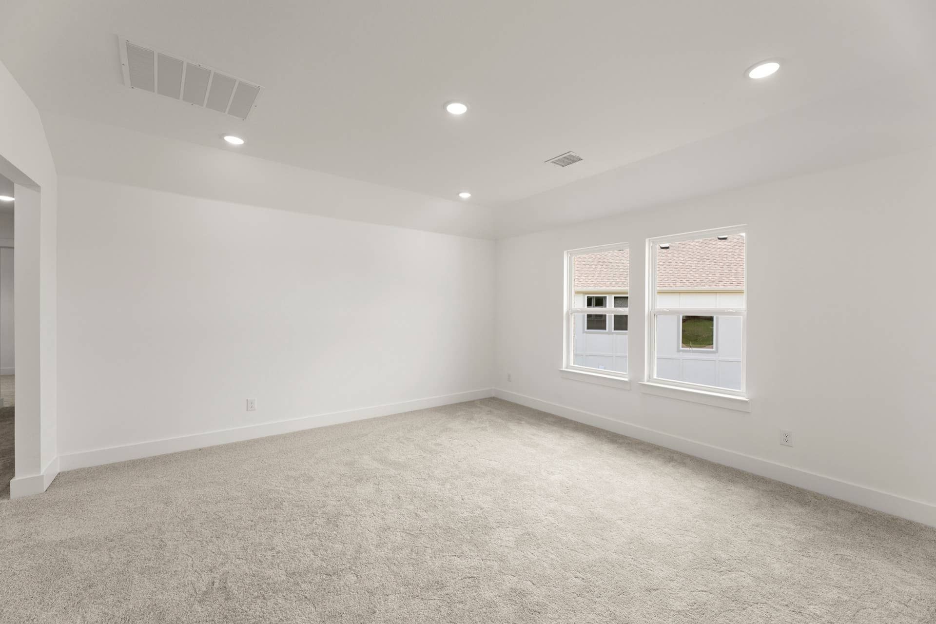 Spacious empty room with carpet flooring and natural light from two windows.
