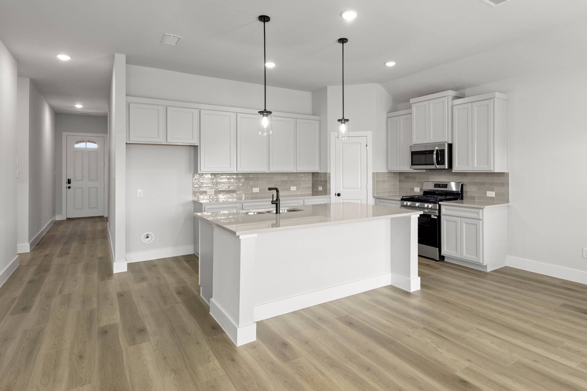 Modern kitchen with island, light wood flooring, and stainless steel appliances.