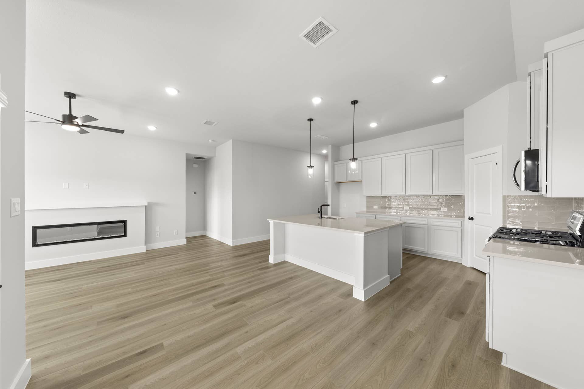 Modern kitchen and living area with hardwood floors and pendant lighting.