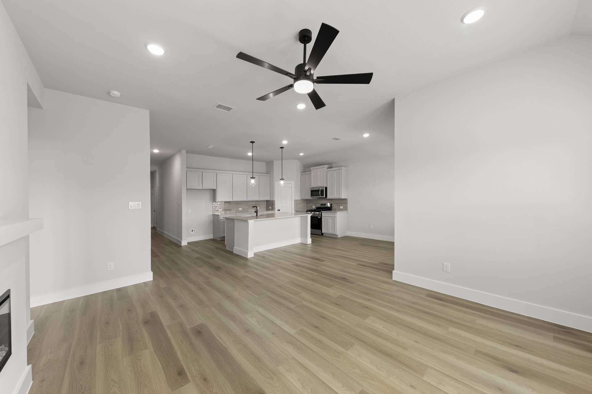 Spacious modern kitchen and living area with hardwood floors and ceiling fan.