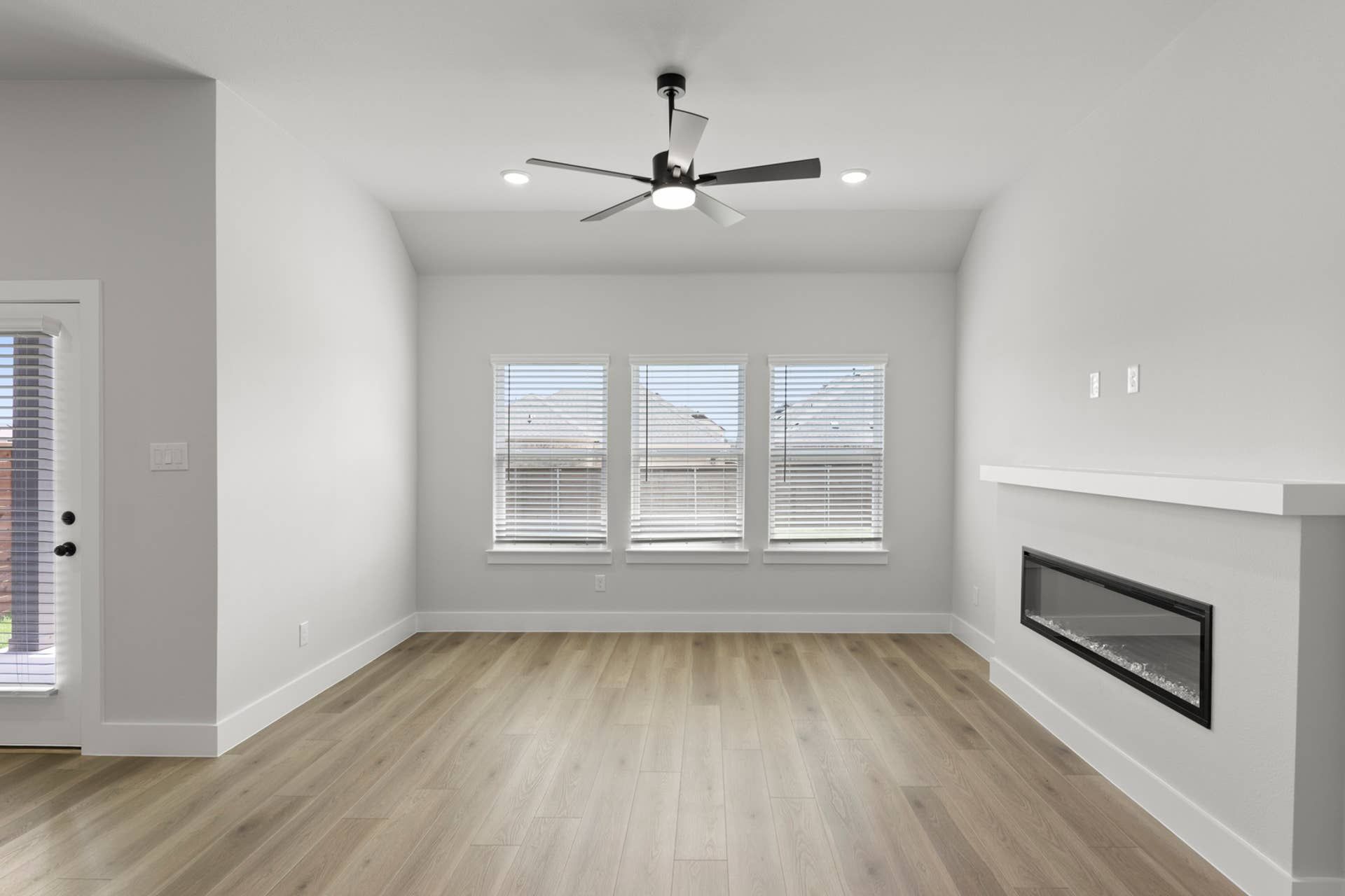Modern living room with ceiling fan, large windows, and sleek electric fireplace.