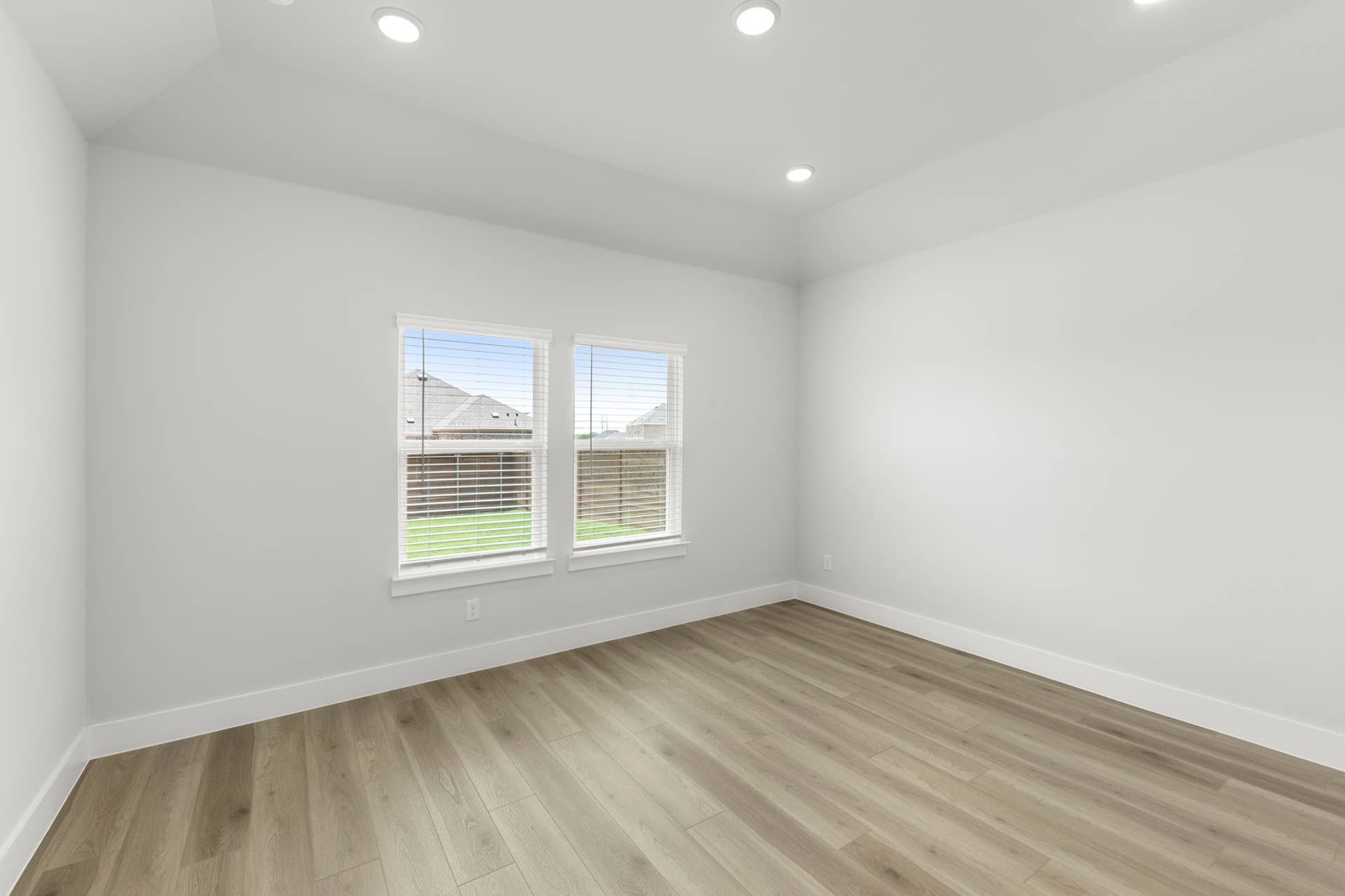 Spacious empty room with hardwood floors and two large windows.
