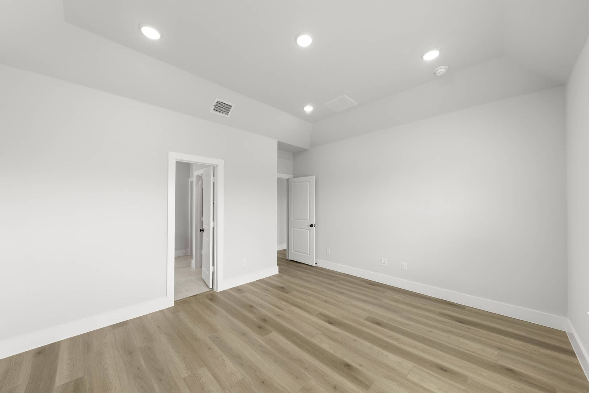 Spacious interior room with hardwood floors and recessed lighting.