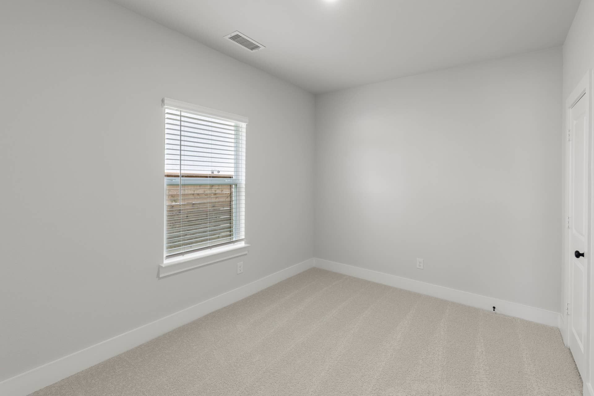 Minimalist bedroom with neutral tones, carpeted floor, and a window with blinds.